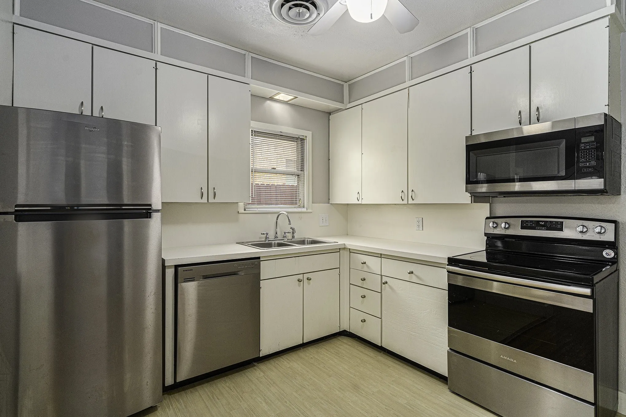 Kitchen with white cabinetry, ceiling fan, stainless steel appliances, sink, and light hardwood / wood-style floors