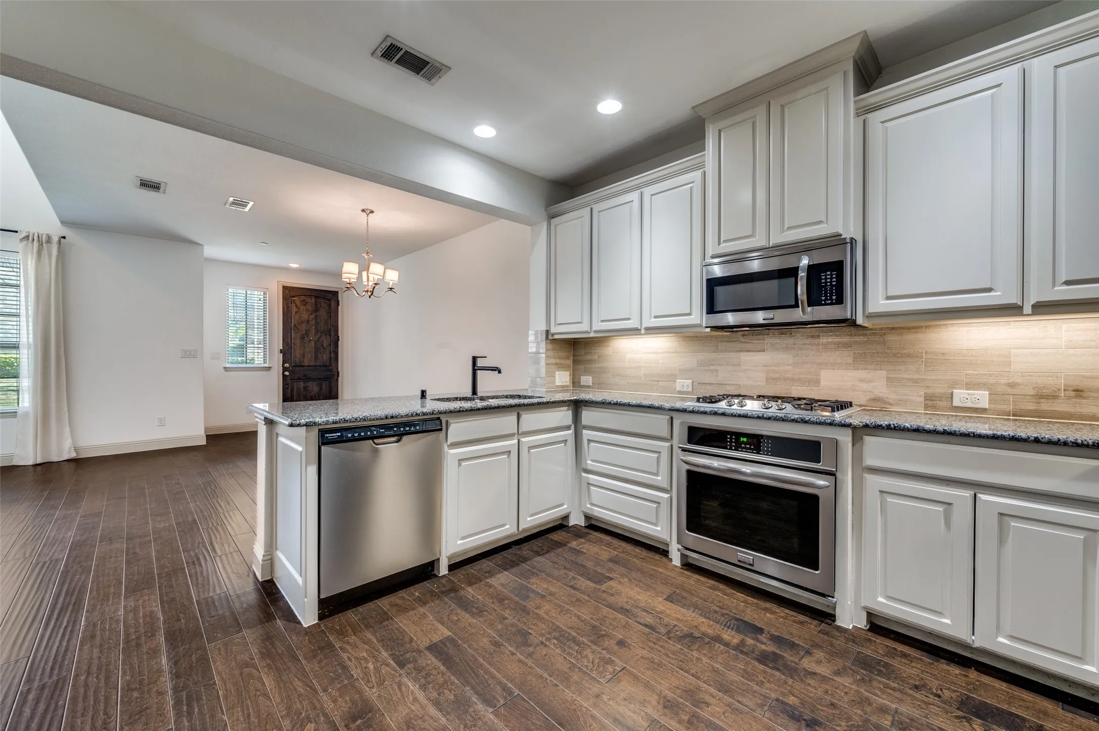 Kitchen with peninsula, light stone counters, stainless steel appliances, chandelier, and open sightlines to the living and dining spaces, creating a functional open kitchen layout that is perfect for casual dining, bar seating, entertaining guests, and everyday family life in this McKinney Texas townhome in North Texas.