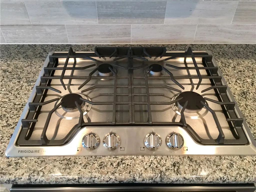Close up of kitchen showing stainless steel gas cooktop, oven, detailed tile backsplash, stone counters, and modern controls, appealing to buyers searching for a McKinney Texas townhouse with stainless steel appliances, gas cooking, and stylish kitchen design in a convenient Collin County location near major roads and retail.