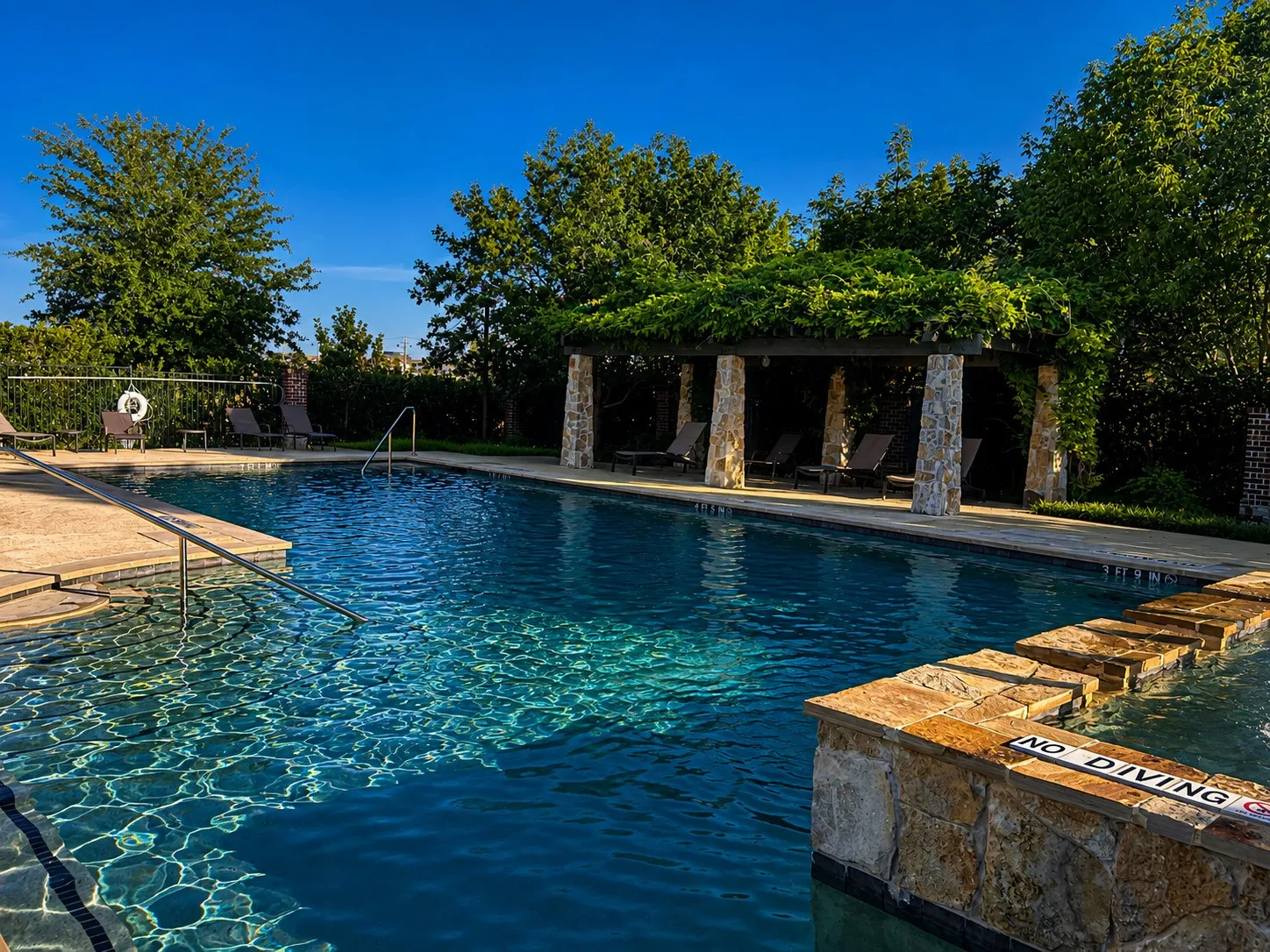 Outdoor swimming pool featuring stone coping, a stone-clad hot tub with step entry, and a covered pergola