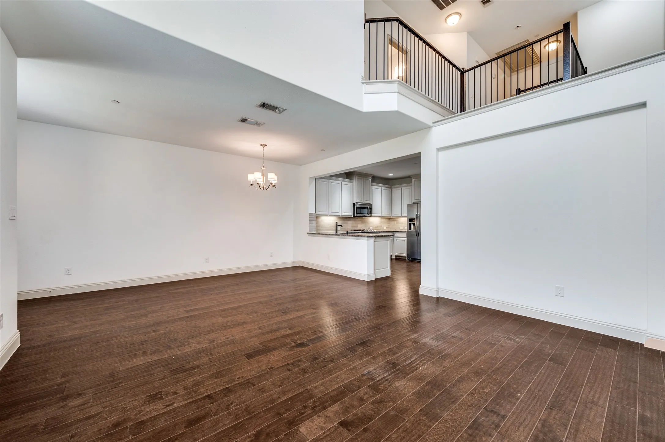 Open living room with suspended lighting, dark wood style floors, high ceiling, and view of upstairs landing, emphasizing the bright open concept floor plan buyers want in a McKinney TX townhome with modern finishes, move in ready condition, and seamless flow from living to dining and kitchen areas in a Collin County two story townhouse.
