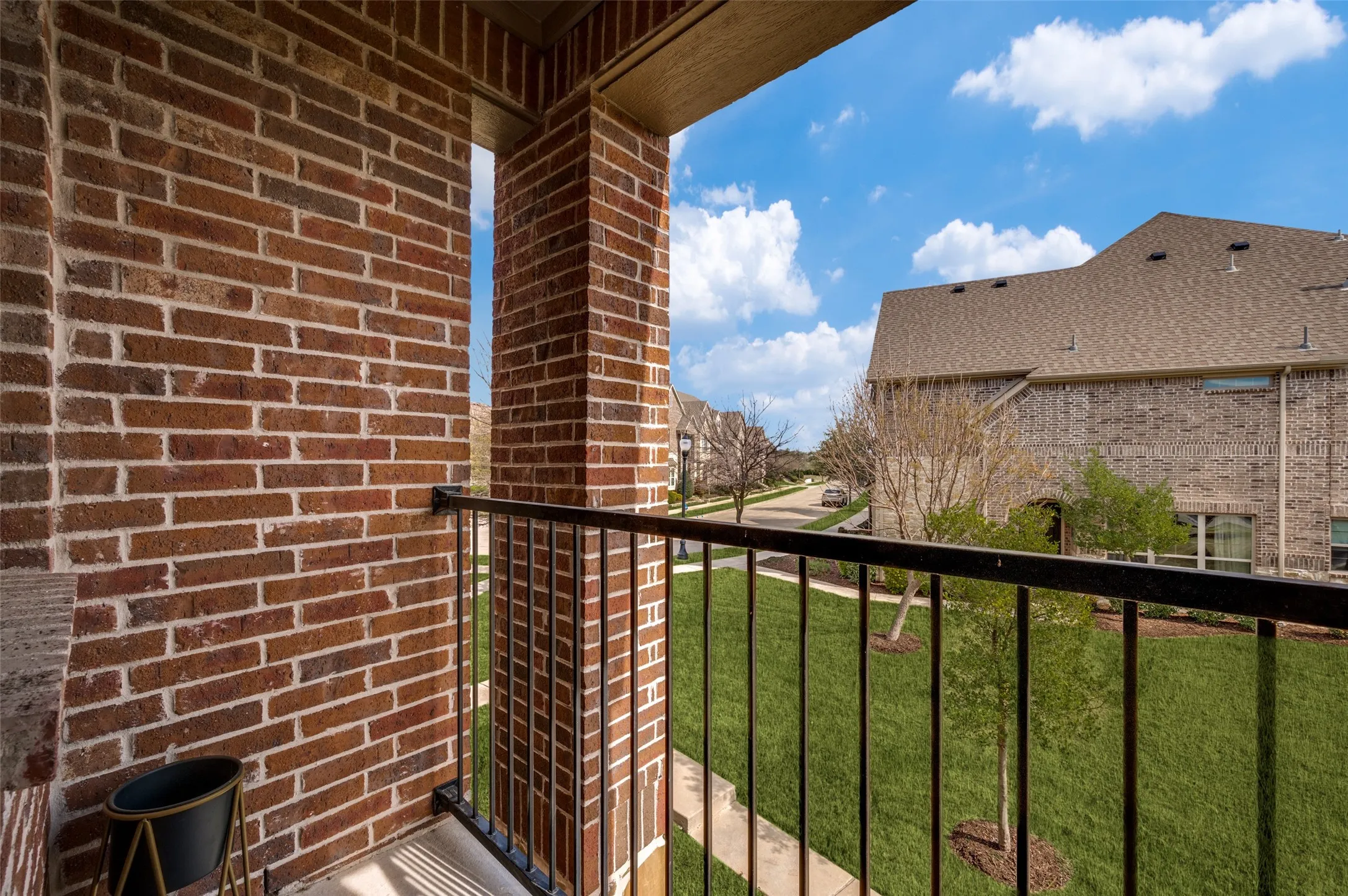 Covered balcony at 7424 Mitchell Drive McKinney Texas with brick surround and iron railing, providing private outdoor living space and neighborhood views, ideal for buyers searching for a McKinney TX townhome with balcony, outdoor seating area, and relaxing spot in a quiet Collin County subdivision.