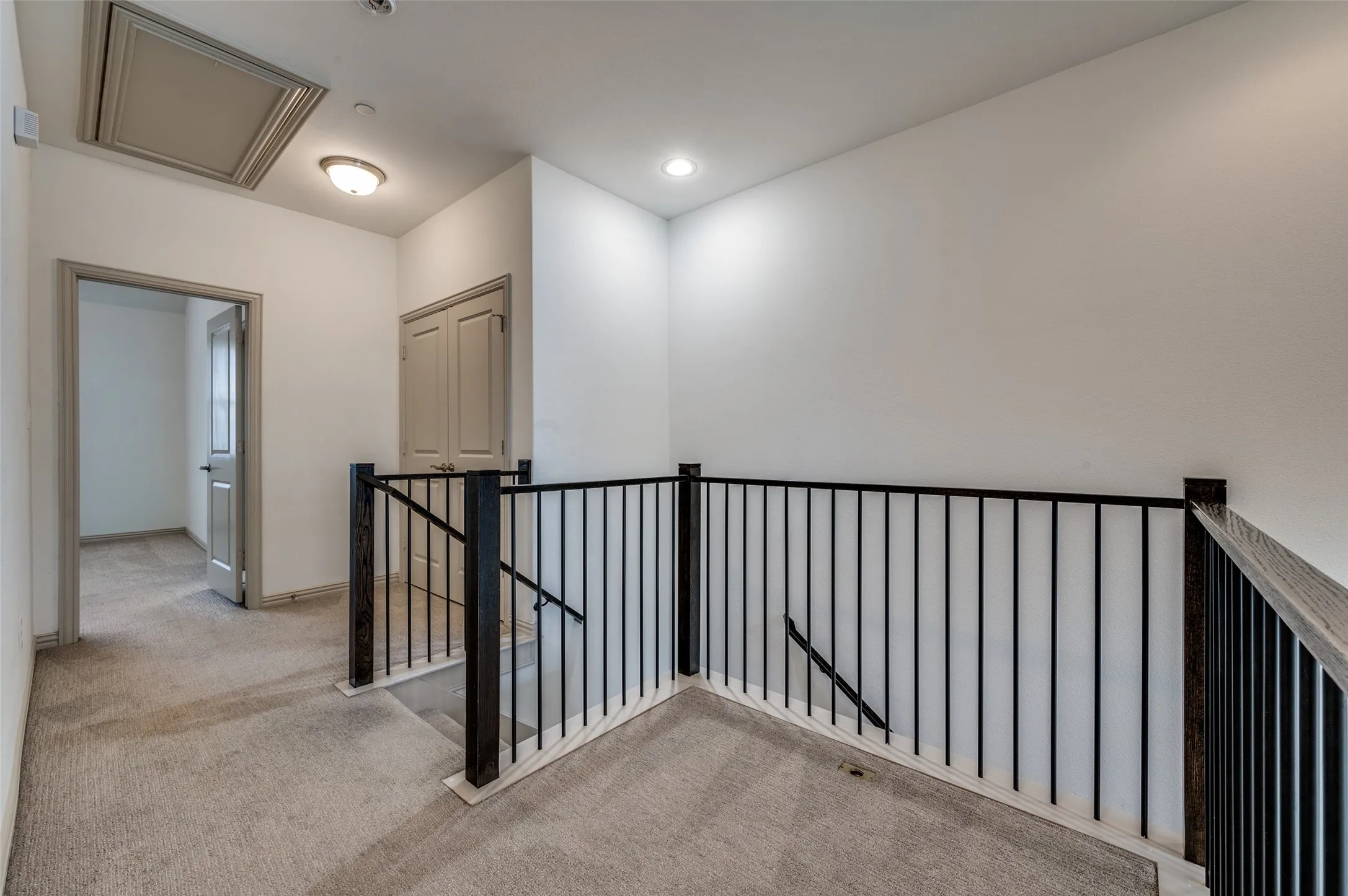 Upstairs hallway with landing, light colored carpet, iron railing, recessed lighting, and access to multiple rooms, connecting bedrooms and living spaces in this McKinney TX townhome for sale and showcasing the open second level layout in a Collin County two story townhouse with functional design.