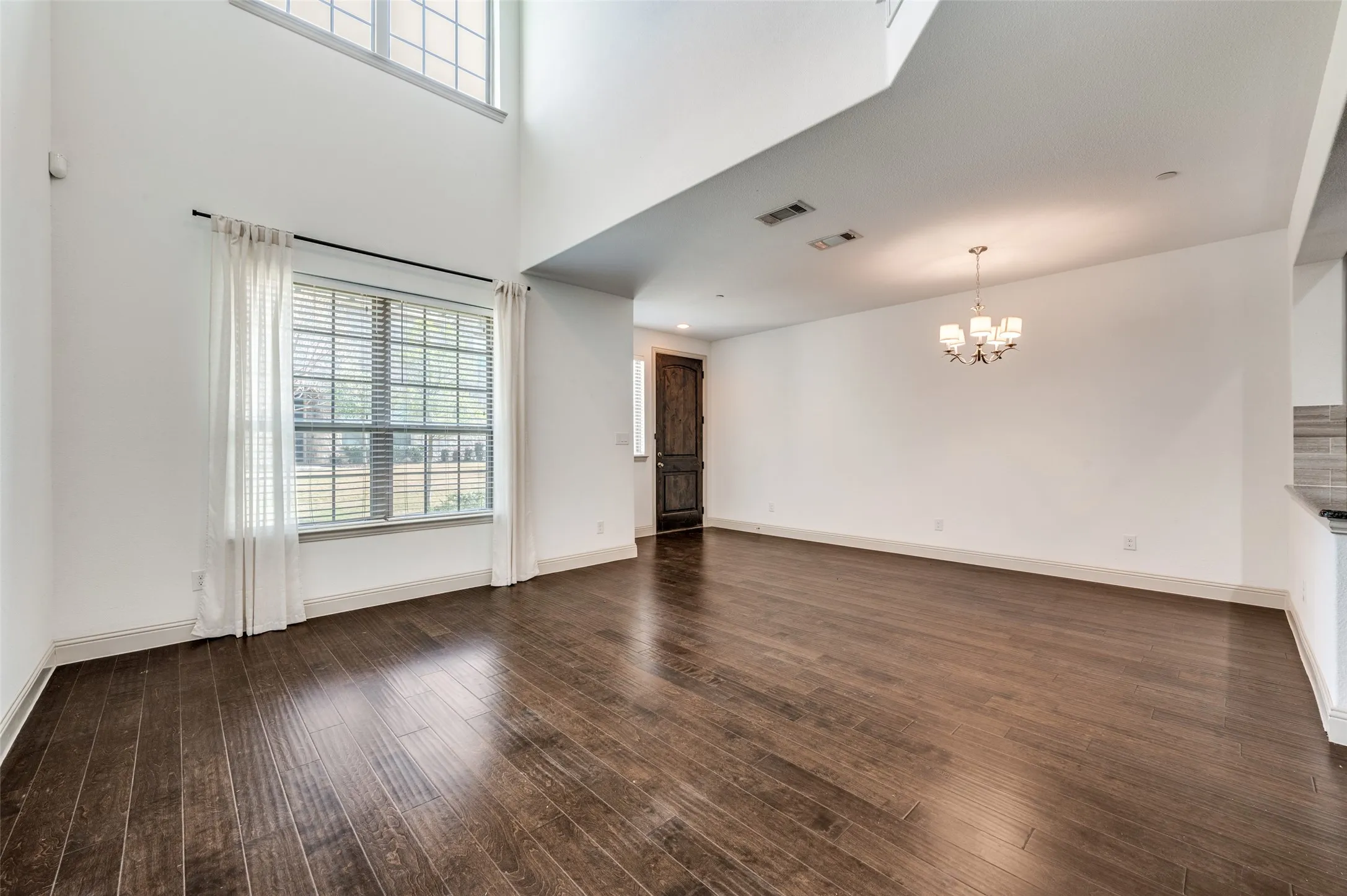 Unfurnished living room in this McKinney TX townhome for sale featuring suspended lighting, soaring high ceiling, dark wood finished floors, neutral wall color, and open concept design, perfect for buyers searching for a modern traditional McKinney townhome with spacious living area, natural light, and room for entertaining in Collin County.