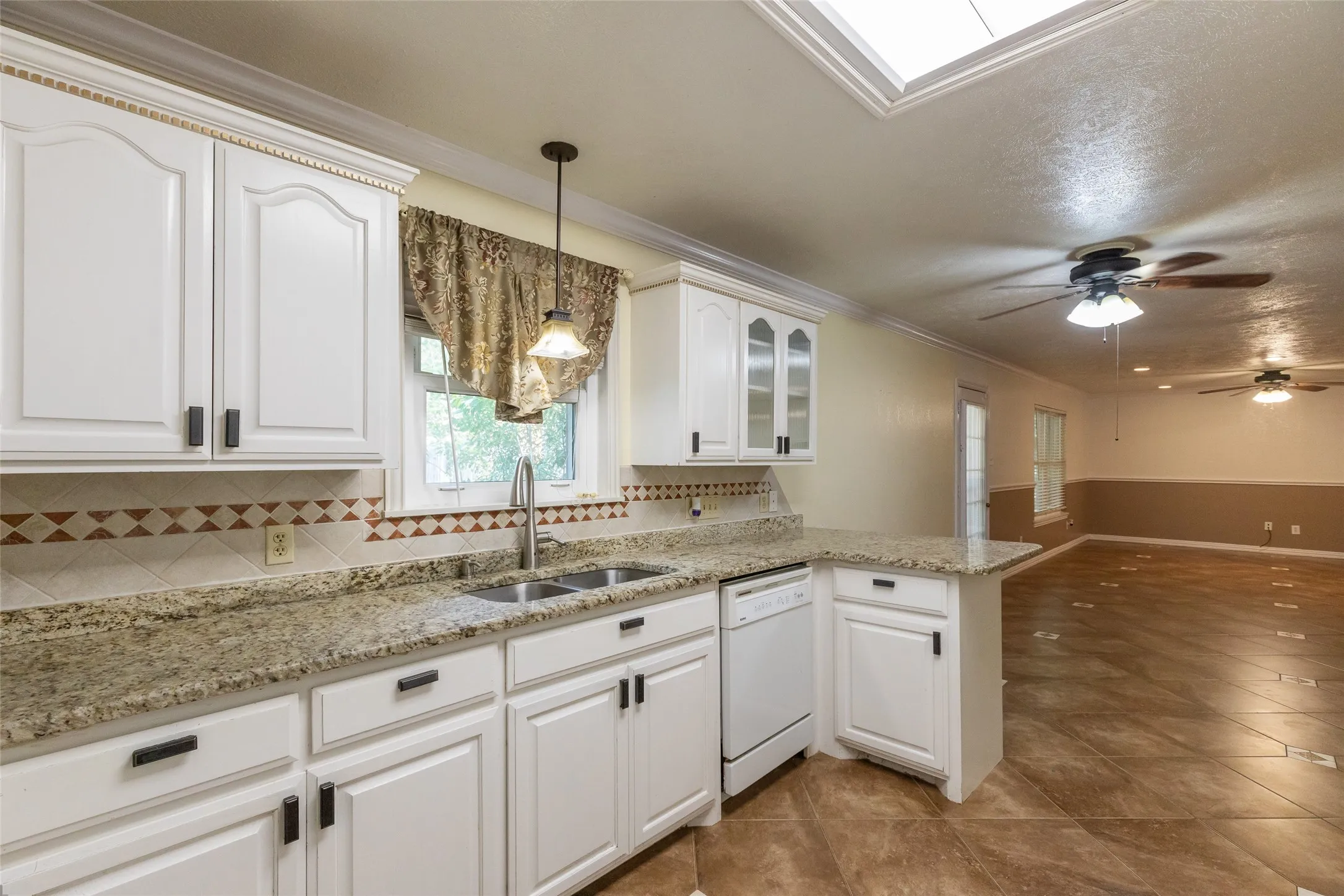 Kitchen featuring white cabinetry with dark hardware, a double basin sink with a gooseneck faucet, light-toned granite countertops, and a tile backsplash