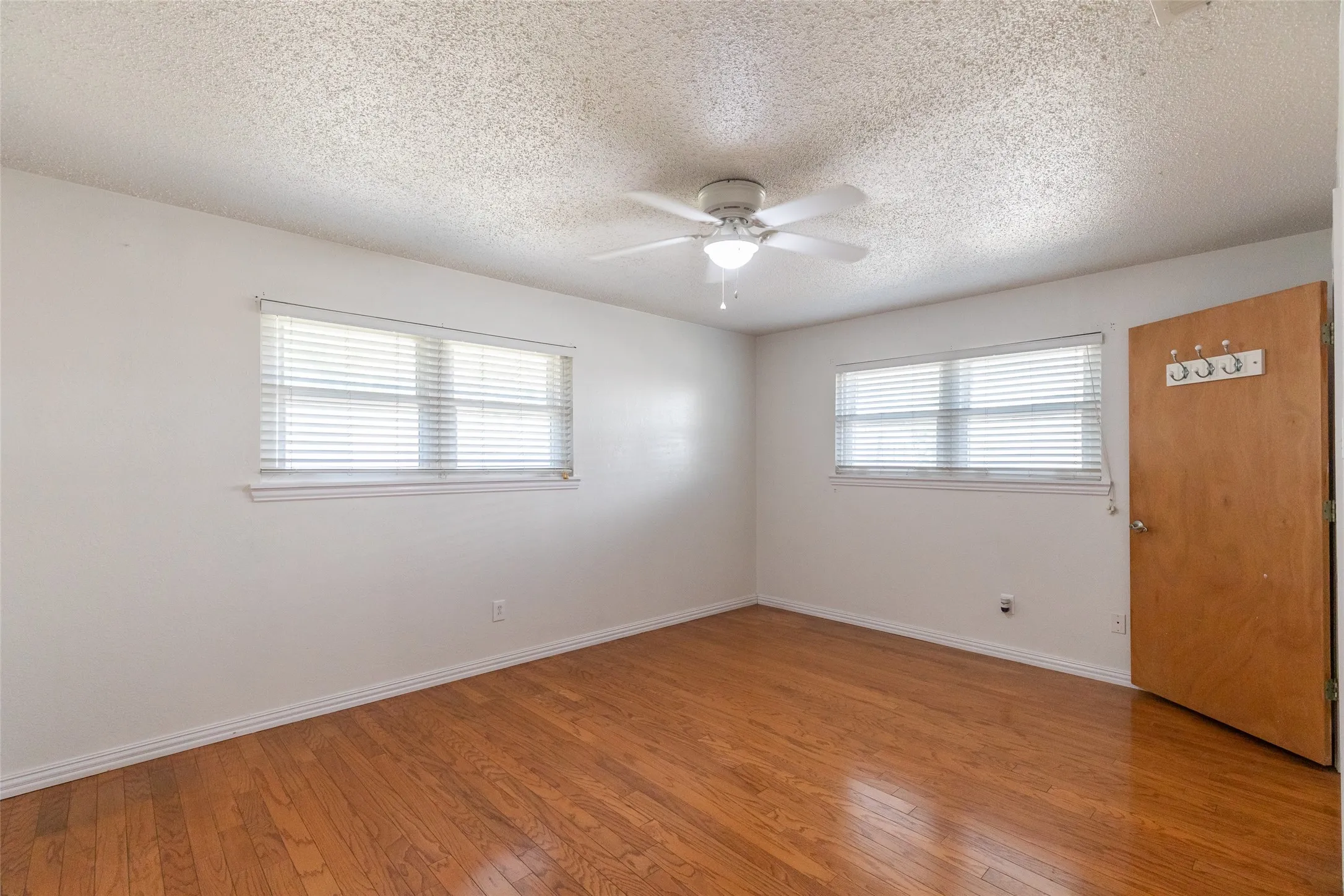 Room featuring wood-finish flooring, white walls, and two windows with blinds