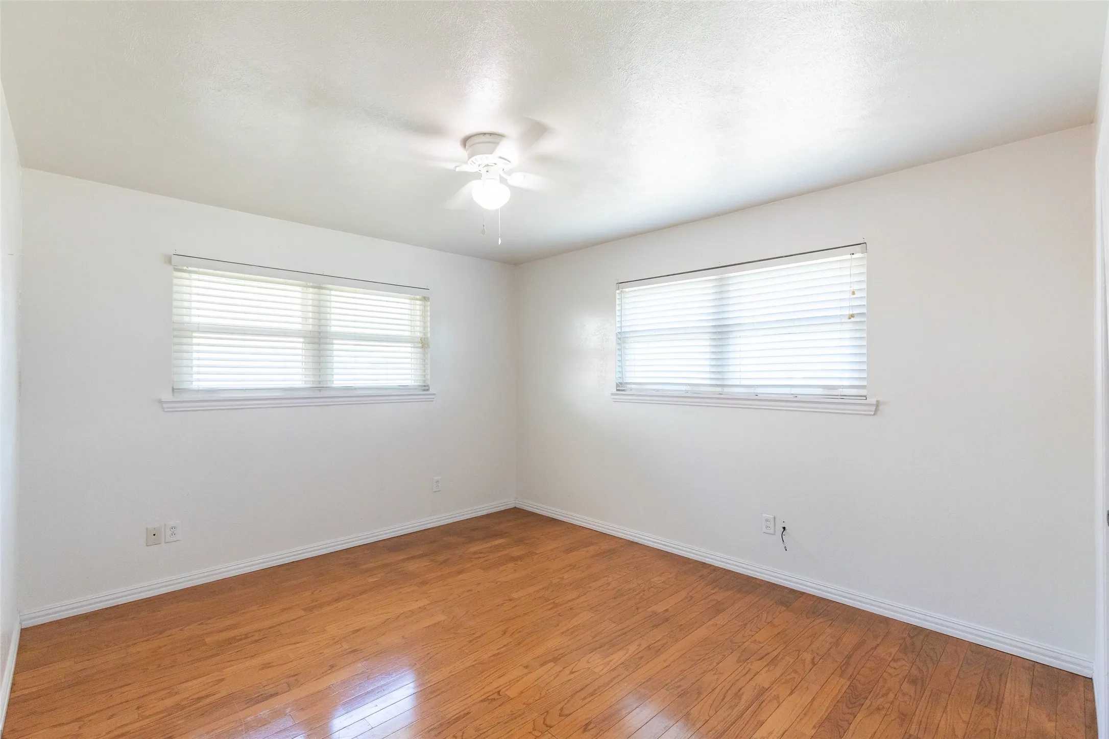 Room featuring wood-finish flooring, white walls, and a ceiling fan
