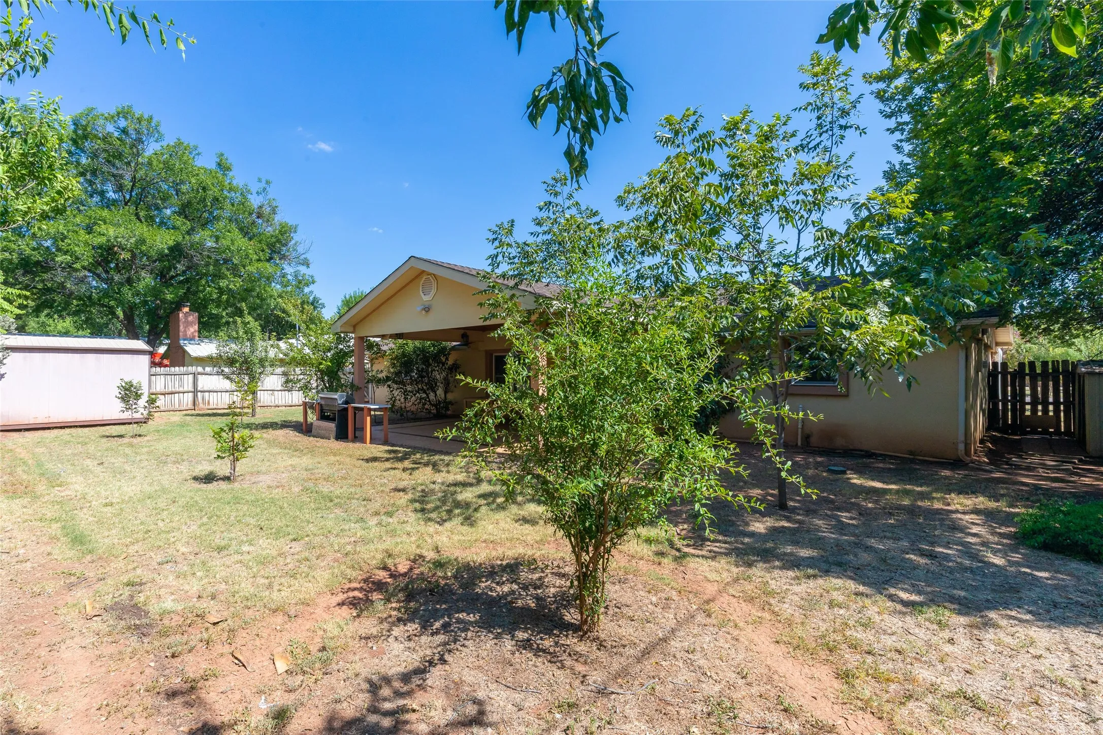 Expansive backyard featuring mature trees, a covered patio area, and a wood privacy fence