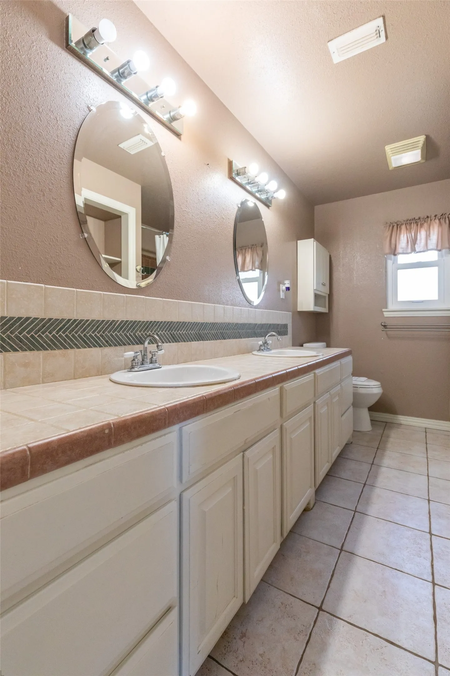 Double vanity featuring two oval mirrors with chrome light fixtures, dual drop-in sinks, and a tiled countertop