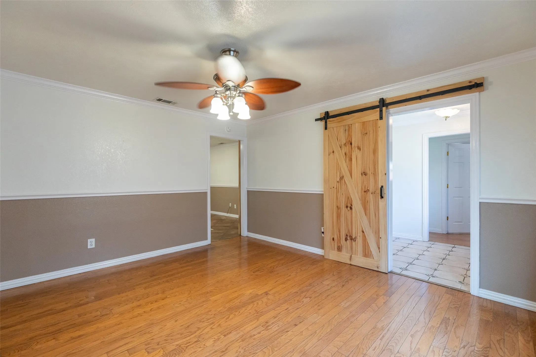 Room featuring wood-finish flooring, two-tone wall paneling, a ceiling fan with integrated lighting, and a prominent barn door