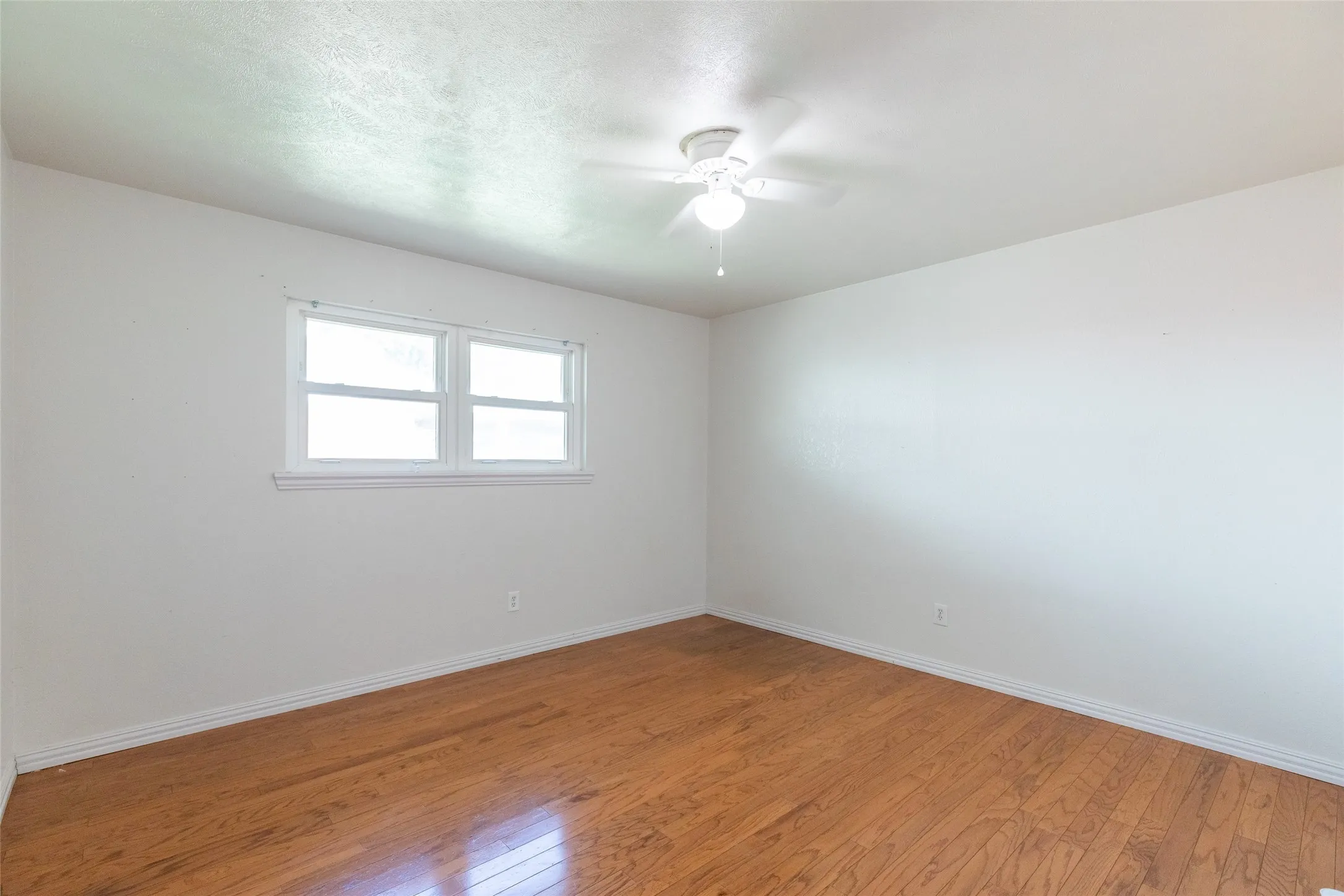 Bright room featuring wood-finish flooring, white walls, and a multi-pane window