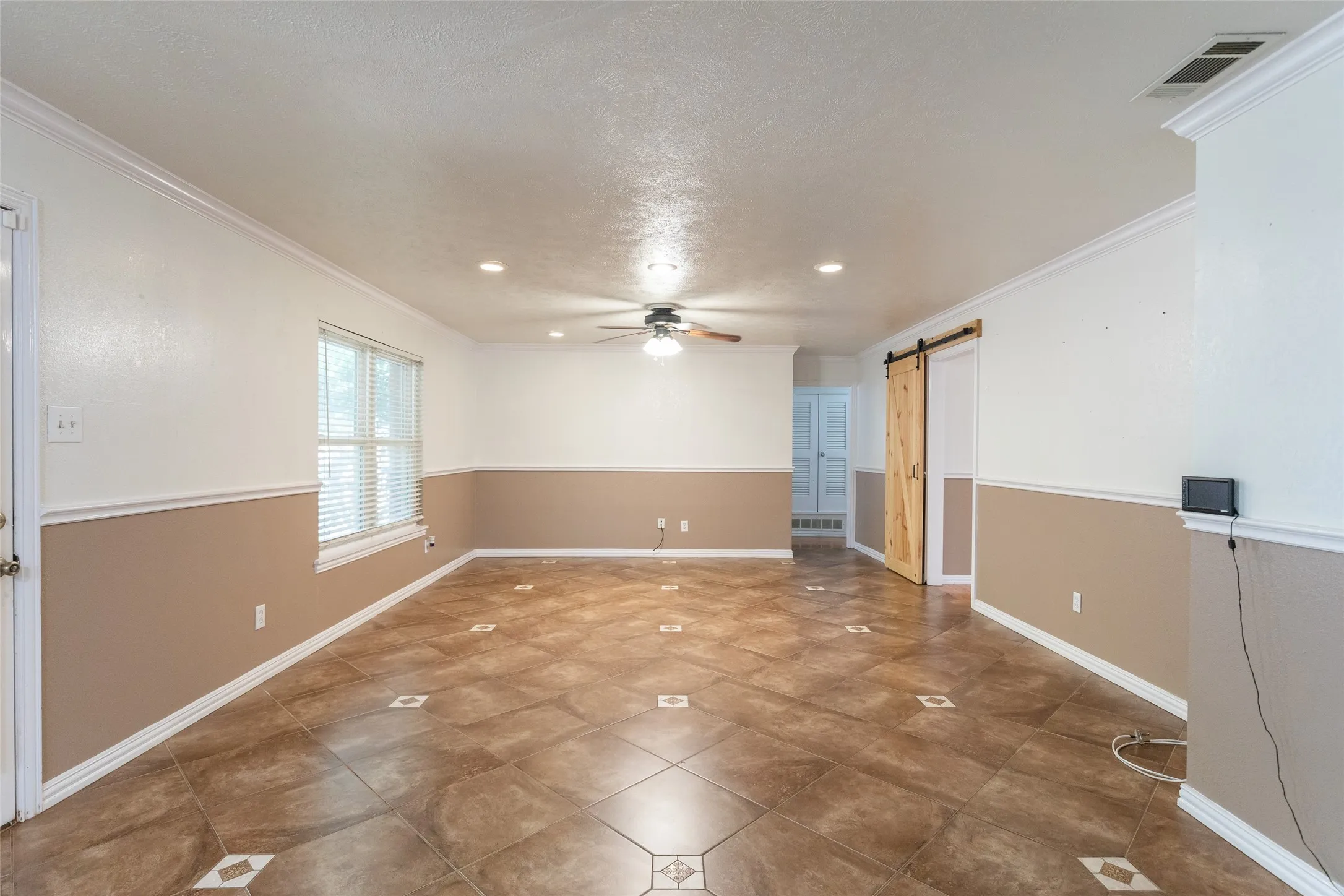 Expansive room with patterned tile flooring, a natural wood barn door, recessed lighting, and a ceiling fan