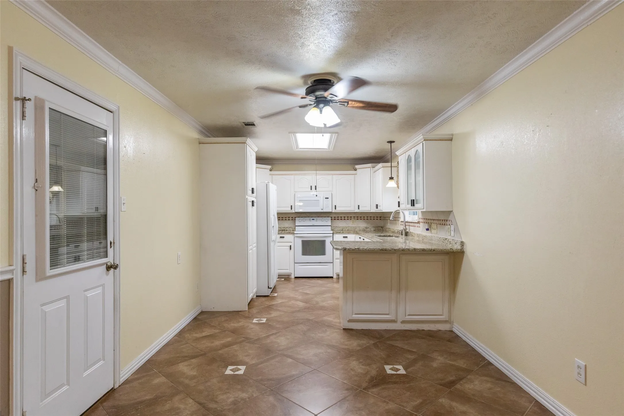 Kitchen and dining area featuring ceramic tile flooring with decorative inserts, a breakfast bar, white cabinetry, a built-in oven, and a ceiling fan