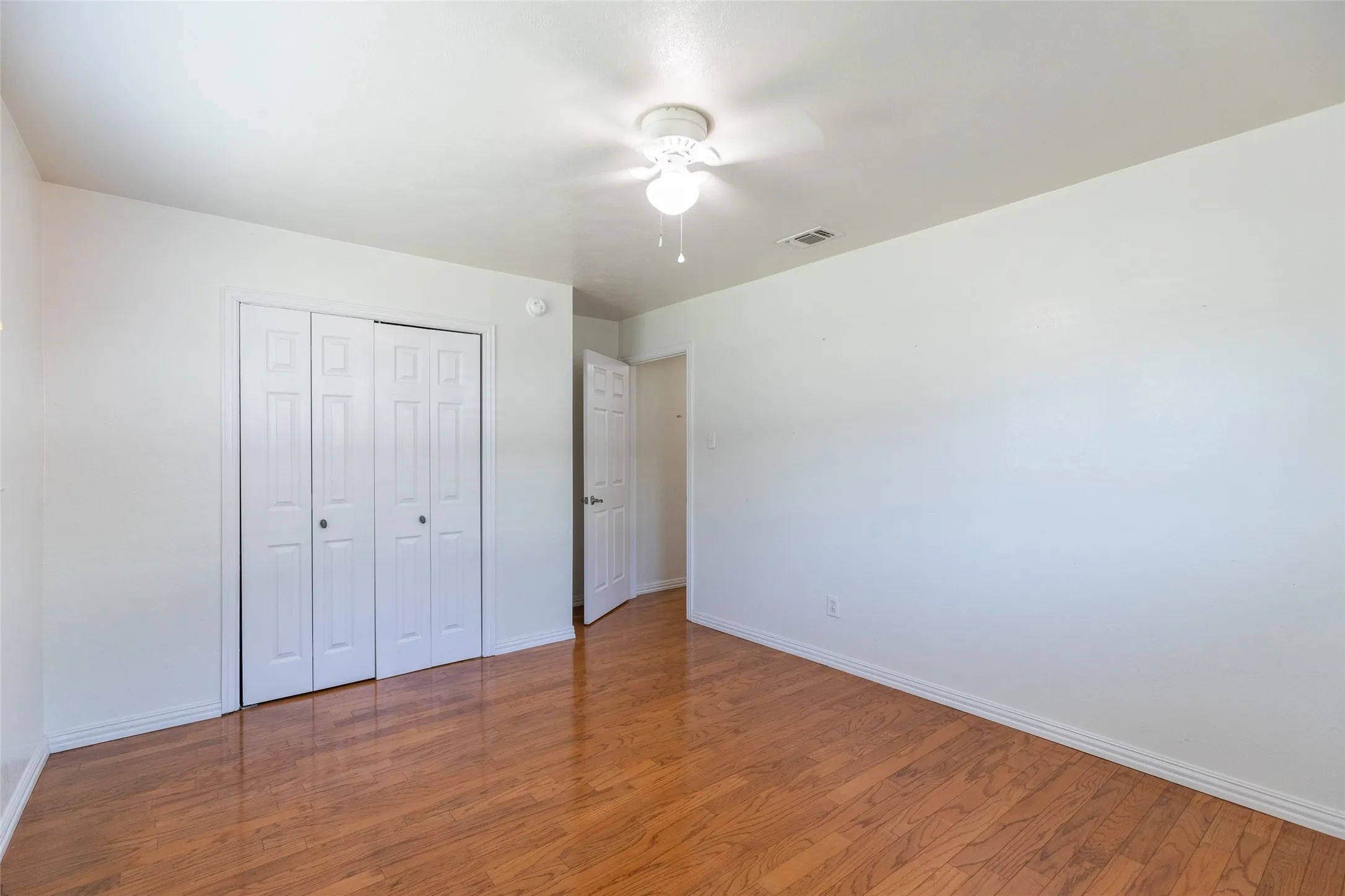 Room featuring wood-finish flooring, white walls, and a ceiling fan with integrated lighting