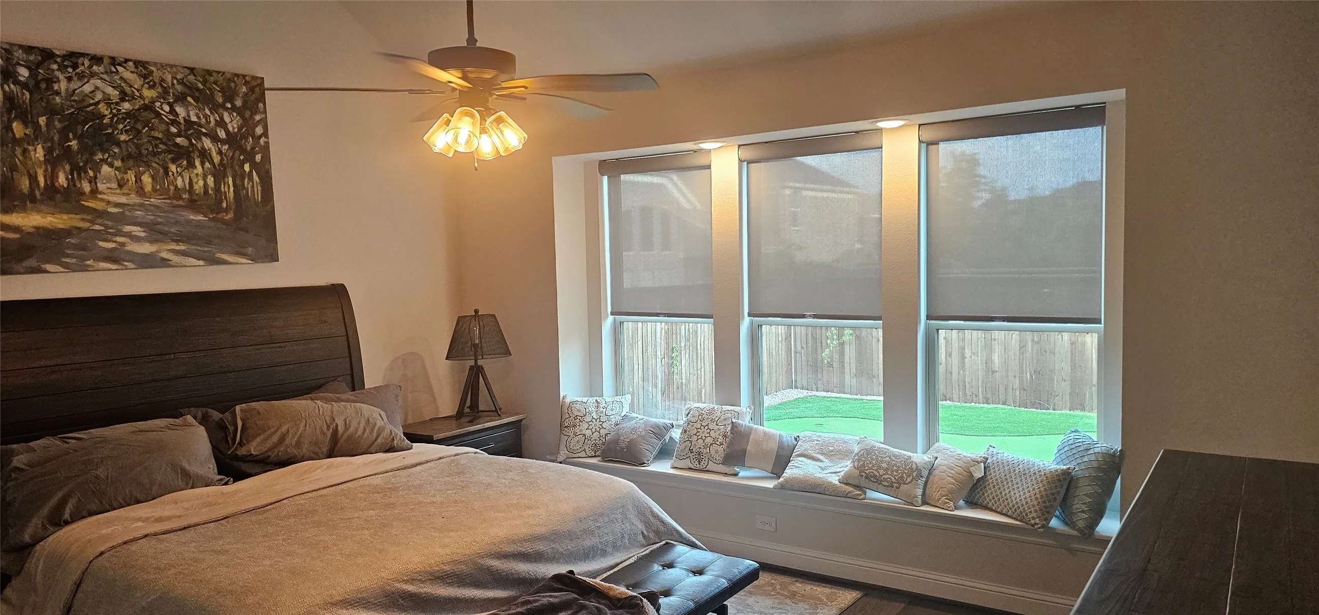 Wood-finish flooring, ceiling fan with integrated lighting, built-in window bench, three large windows with roller shades, and recessed lighting