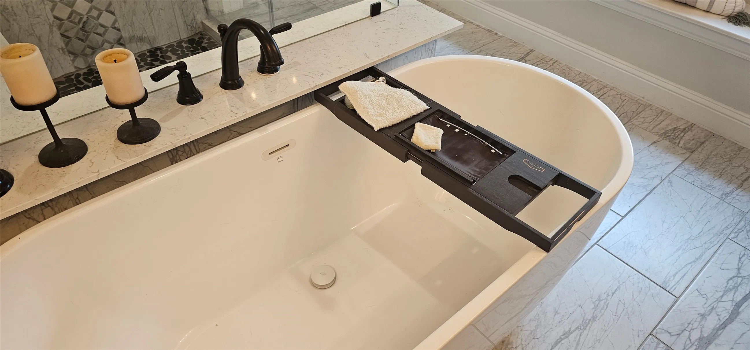 Freestanding soaking tub with a dark bronze faucet, integrated quartz tub deck, and a tiled accent wall