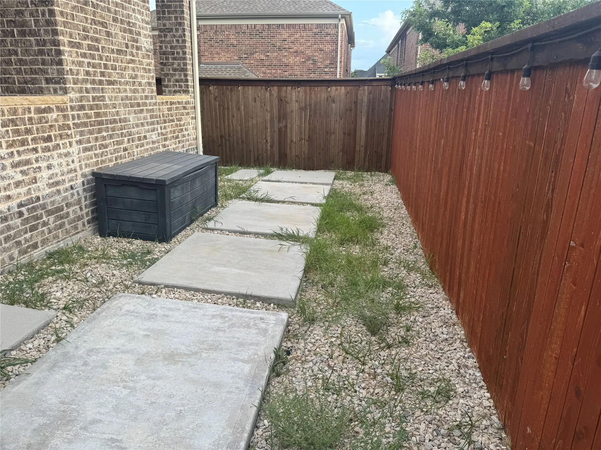 Paved walkway with stone aggregate, brick exterior, and a wood fence