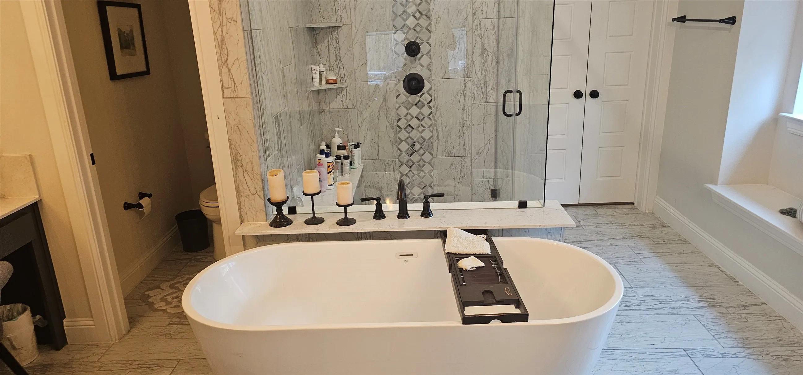 Freestanding soaking tub, walk-in shower with glass enclosure, marble-style tile, and dark bronze fixtures