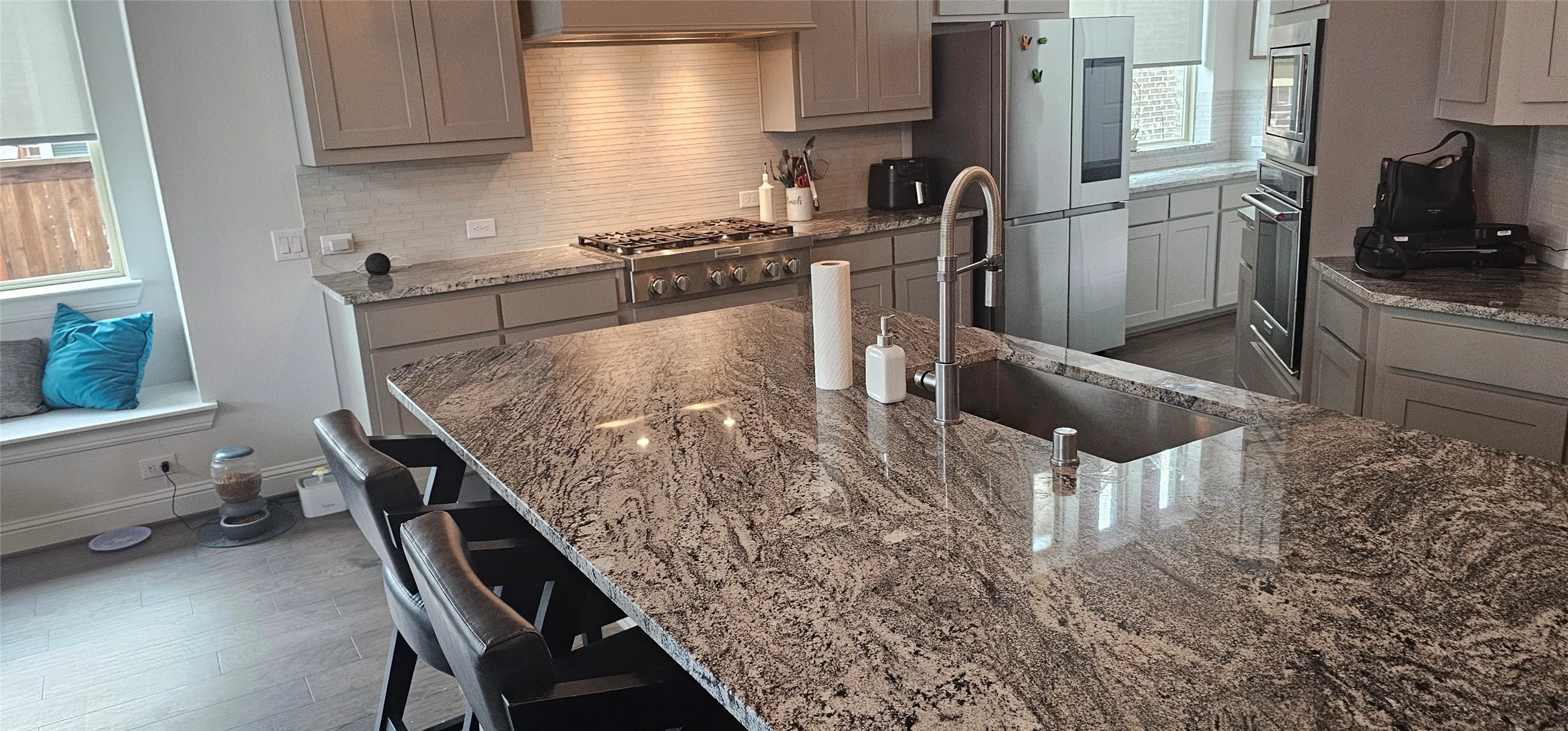 Spacious kitchen island with an undermount sink, granite countertops, light gray cabinetry, and stainless steel appliances