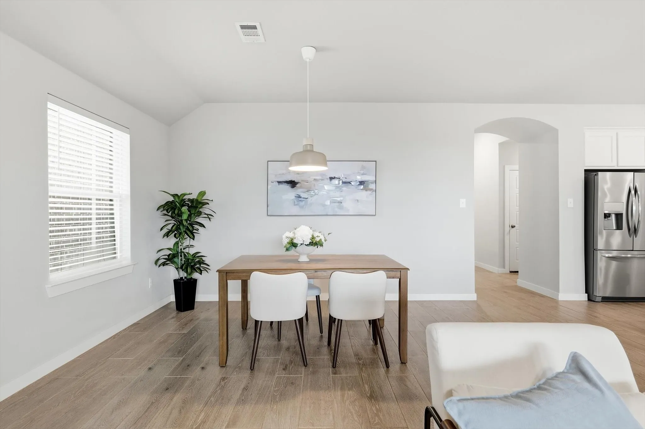 Dining area featuring wood-finish flooring, a contemporary pendant light fixture, and an arched doorway