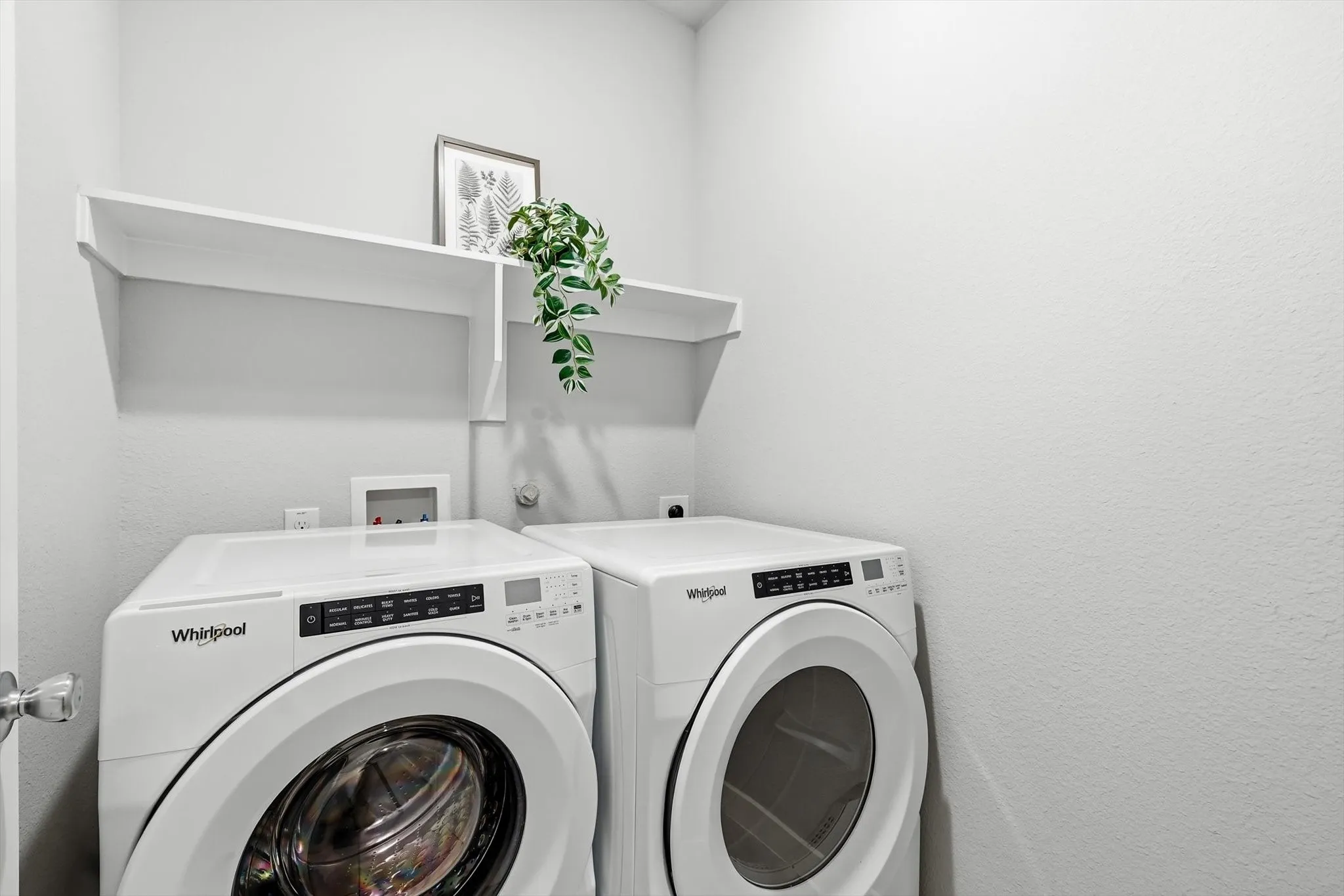 Dedicated laundry space featuring a side-by-side washer and dryer option, an overhead white storage shelf, and light gray wall finishes!
