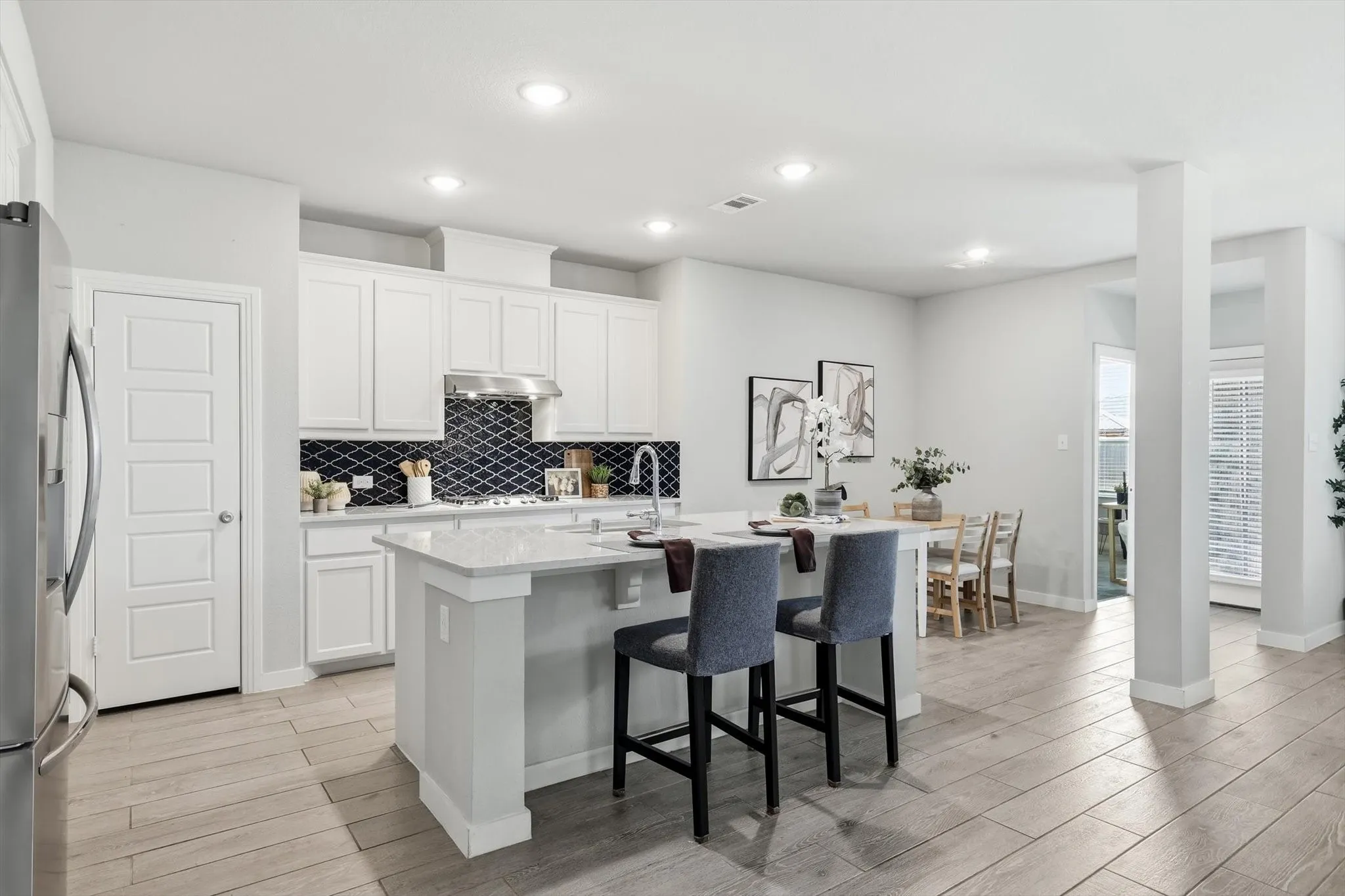 Modern kitchen featuring white cabinetry, a dark patterned tile backsplash, stainless steel appliances, a center island with countertop seating, and recessed lighting