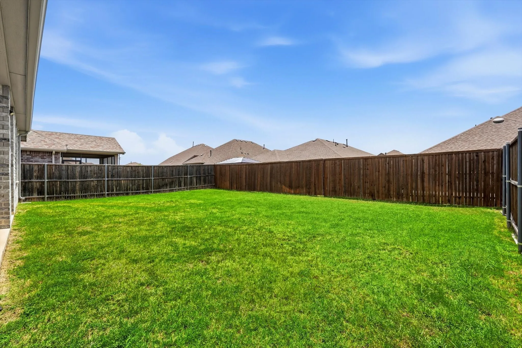 Expansive backyard featuring a lush green lawn, full privacy fencing, and a concrete patio space