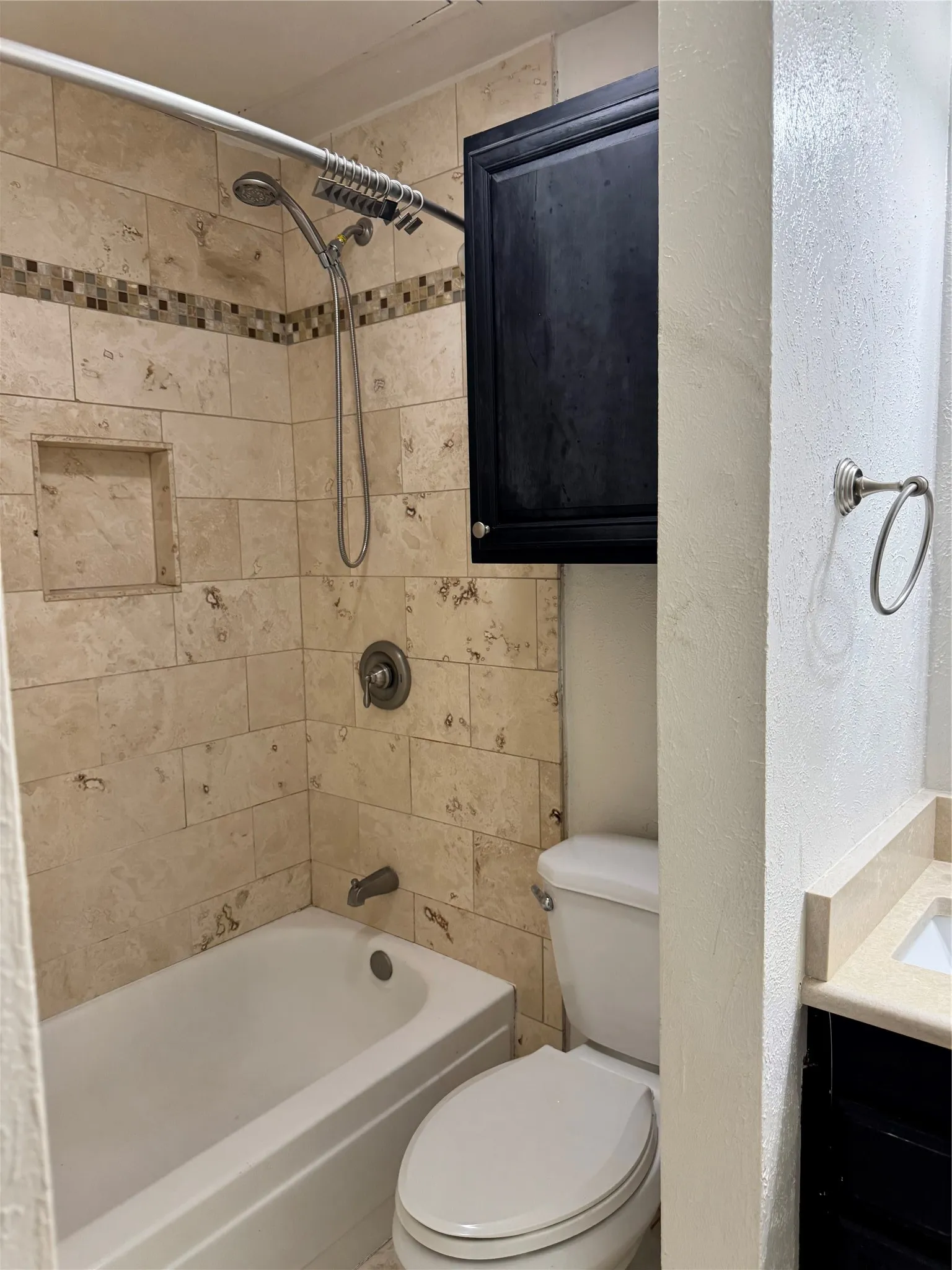Bathtub with a multi-function shower head, tiled shower surround with accent band and built-in niche, and wall-mounted storage cabinet