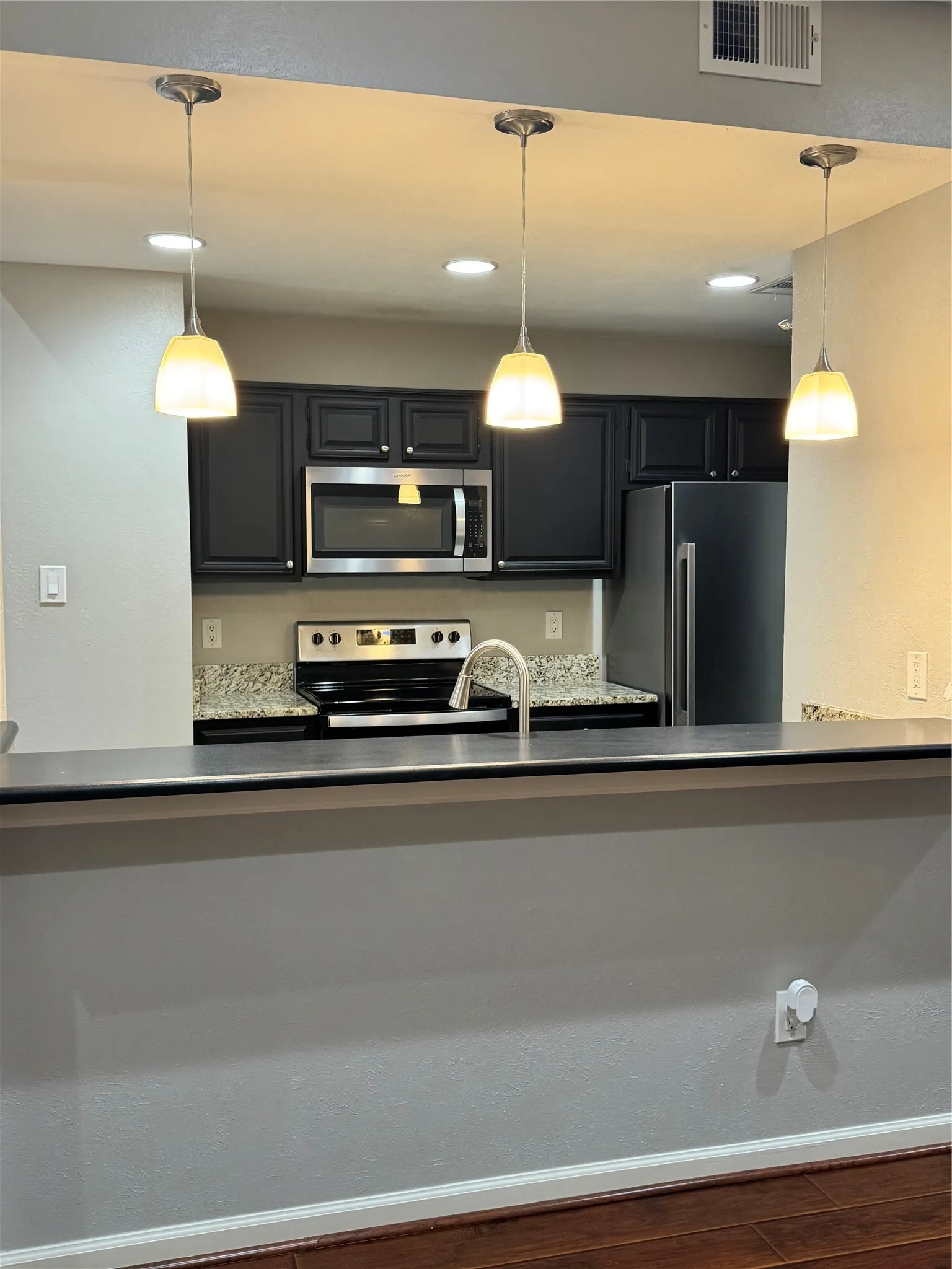Kitchen featuring dark cabinetry, stainless steel appliances, speckled countertops, and pendant lighting
