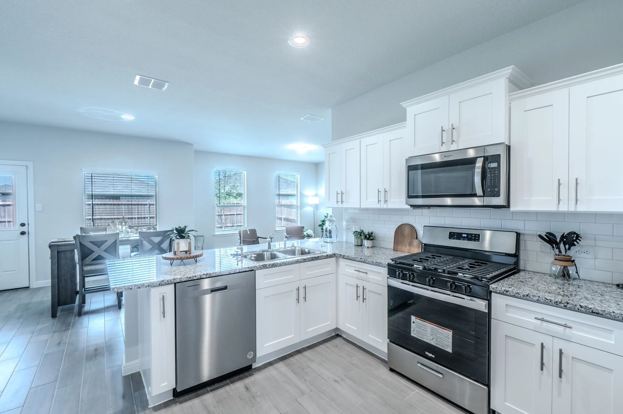 Bright kitchen featuring white shaker cabinetry, stainless steel appliances, speckled stone countertops, and a subway tile backsplash