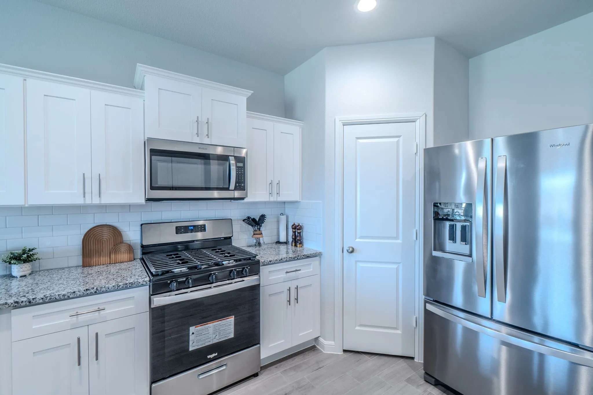 Kitchen featuring white shaker cabinetry, stainless steel appliances, speckled countertops, a white subway tile backsplash, and light wood-finish flooring