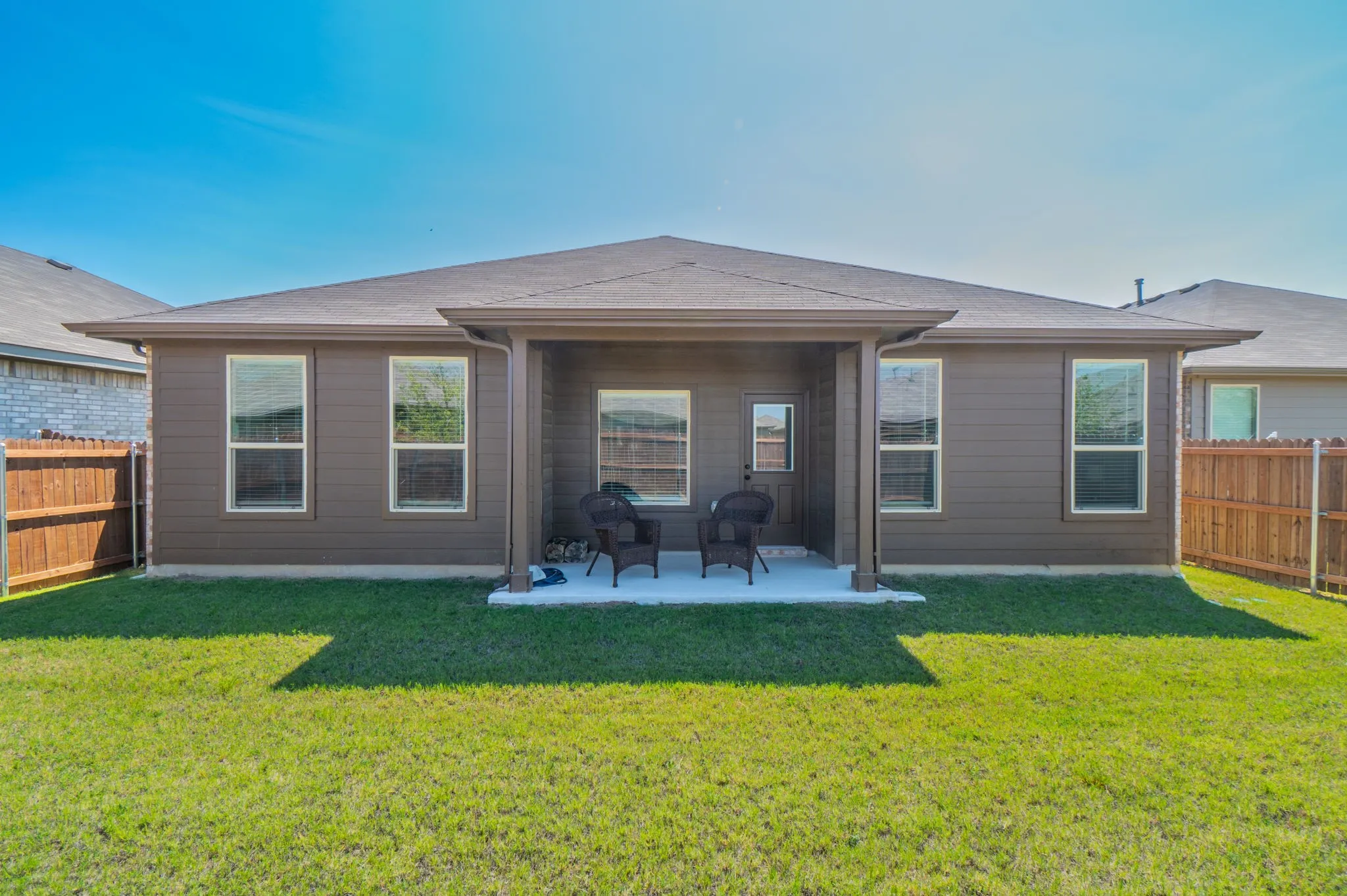 Expansive backyard featuring a manicured lawn, full privacy fencing, and a covered patio with a concrete surface