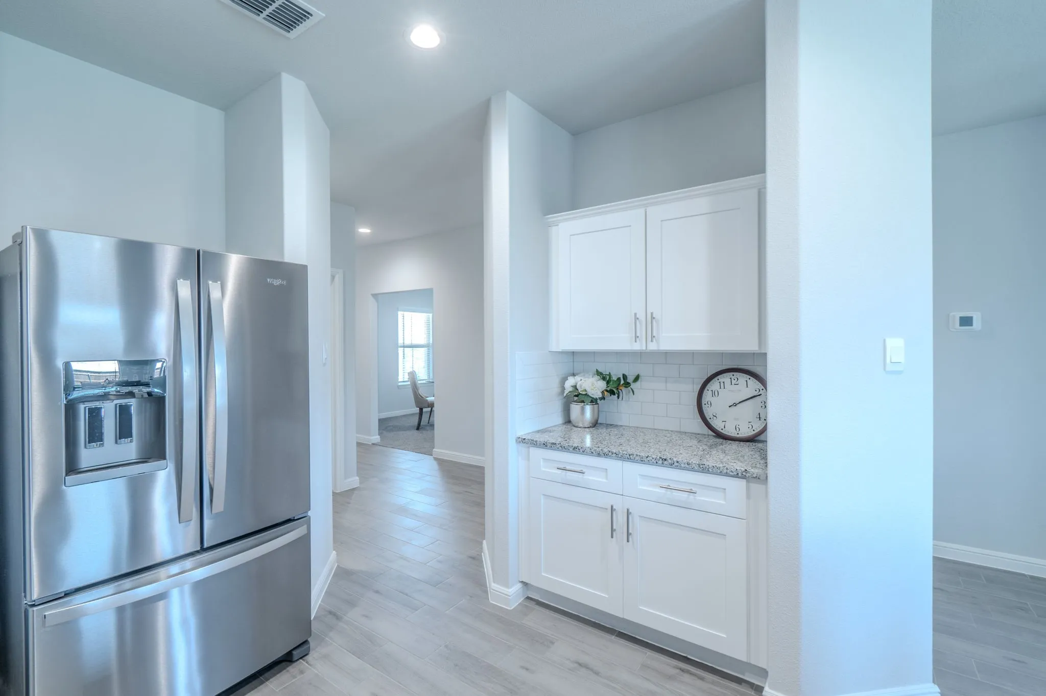 Stainless steel French door refrigerator, white shaker-style cabinetry, granite-finish countertop, subway tile backsplash, and wood-finish flooring