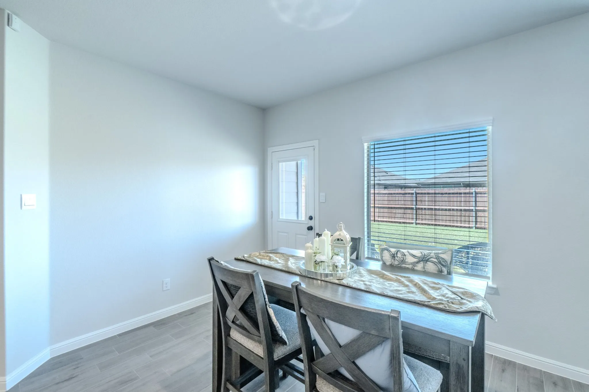Bright interior space featuring wood-finish flooring, a rear exterior door with a glass pane, and a large window with horizontal blinds