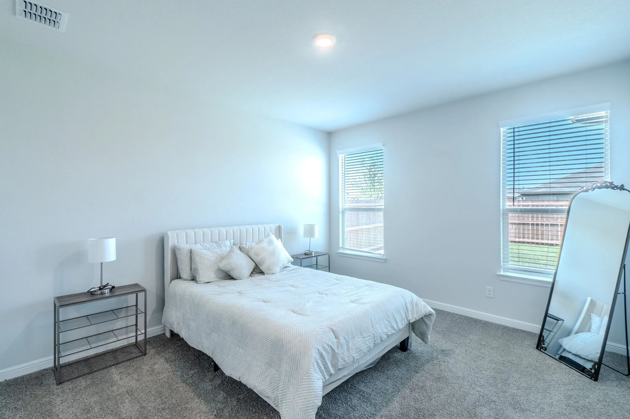 Carpeted bedroom with two windows featuring blinds, neutral painted walls, and a recessed ceiling light