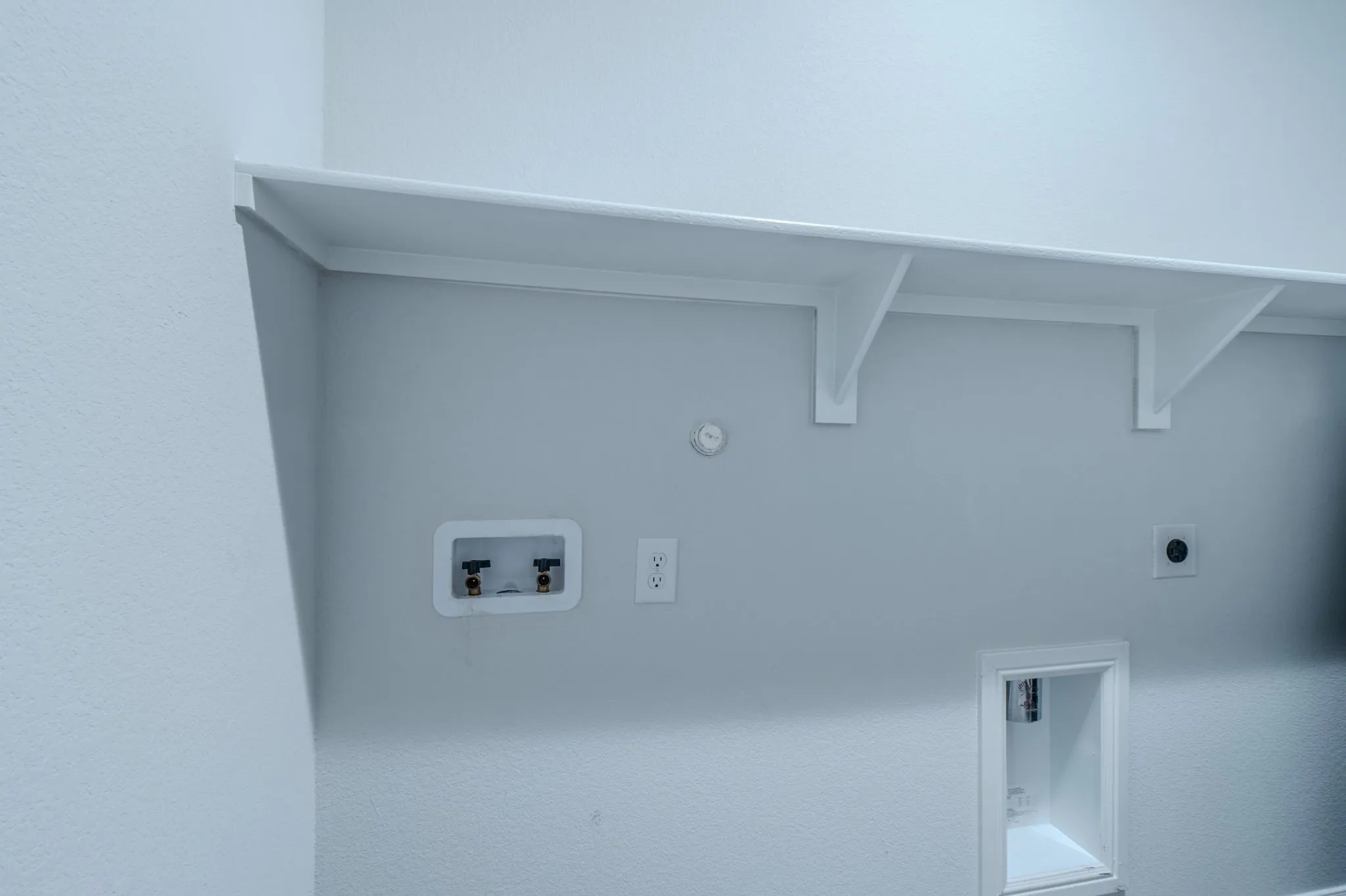 Laundry area featuring a white wall shelf, utility hookups, and a standard electrical outlet