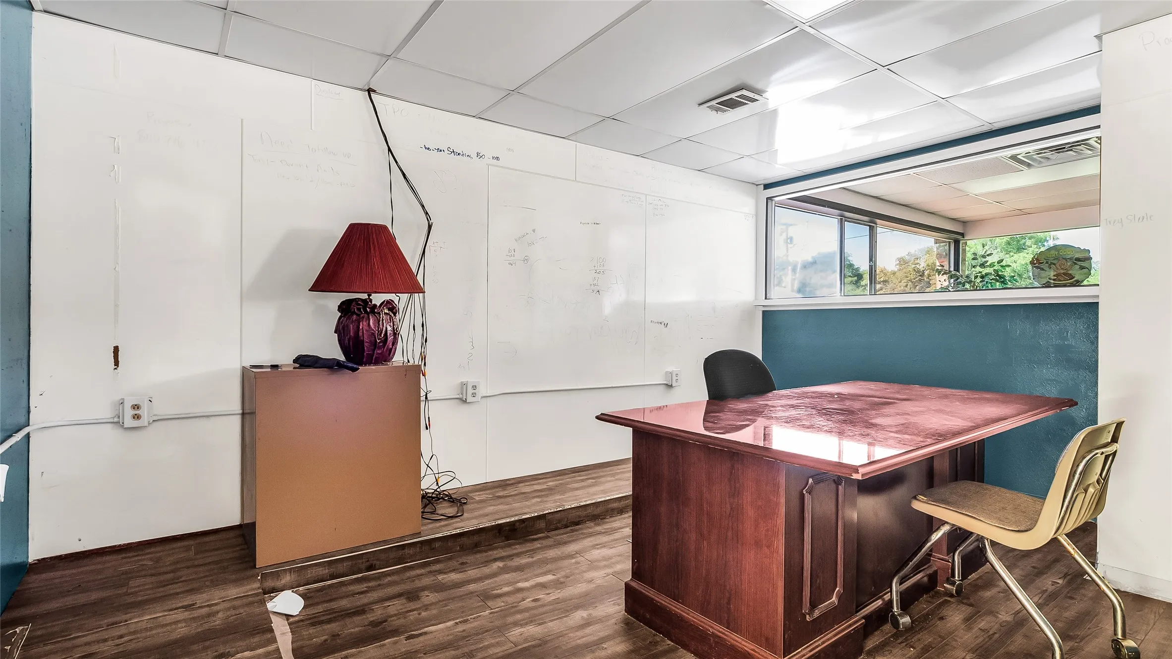 Wood-finish flooring with white wall panels, a drop ceiling, and a large interior window