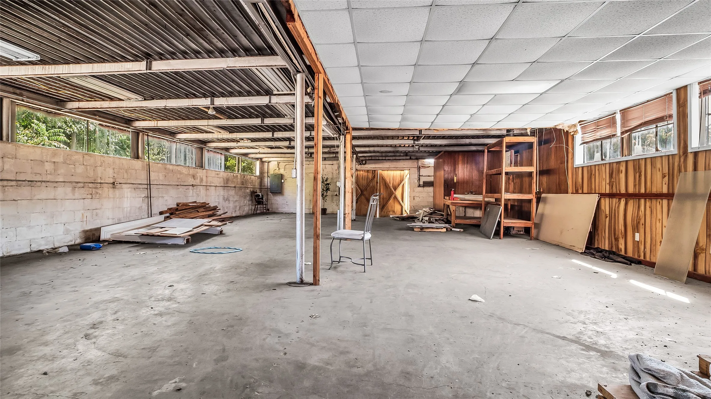 Spacious open area featuring concrete flooring, a drop ceiling, and wood paneling