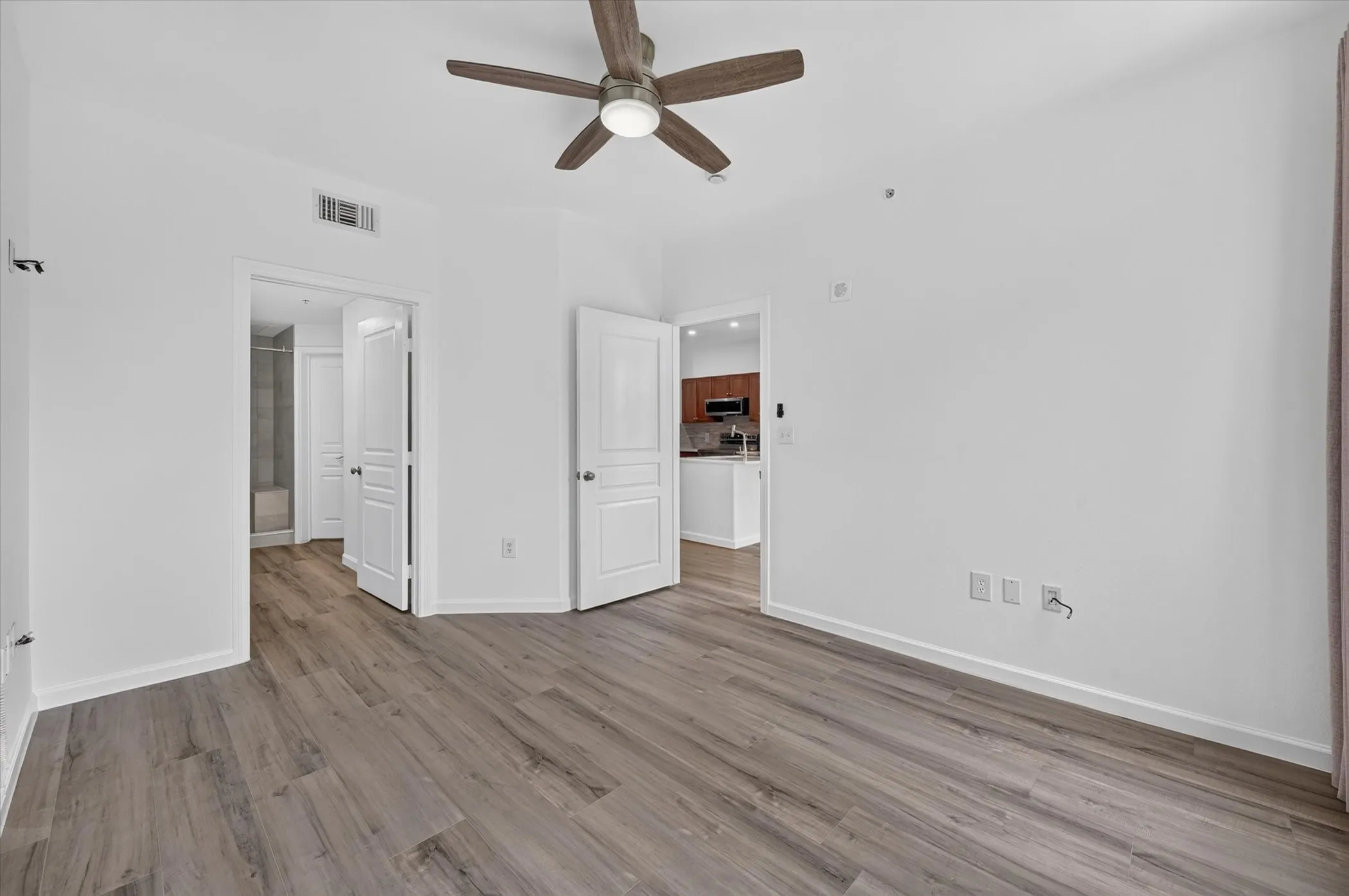 Spacious room featuring wood-finish flooring, a ceiling fan with integrated lighting, and multiple doorways