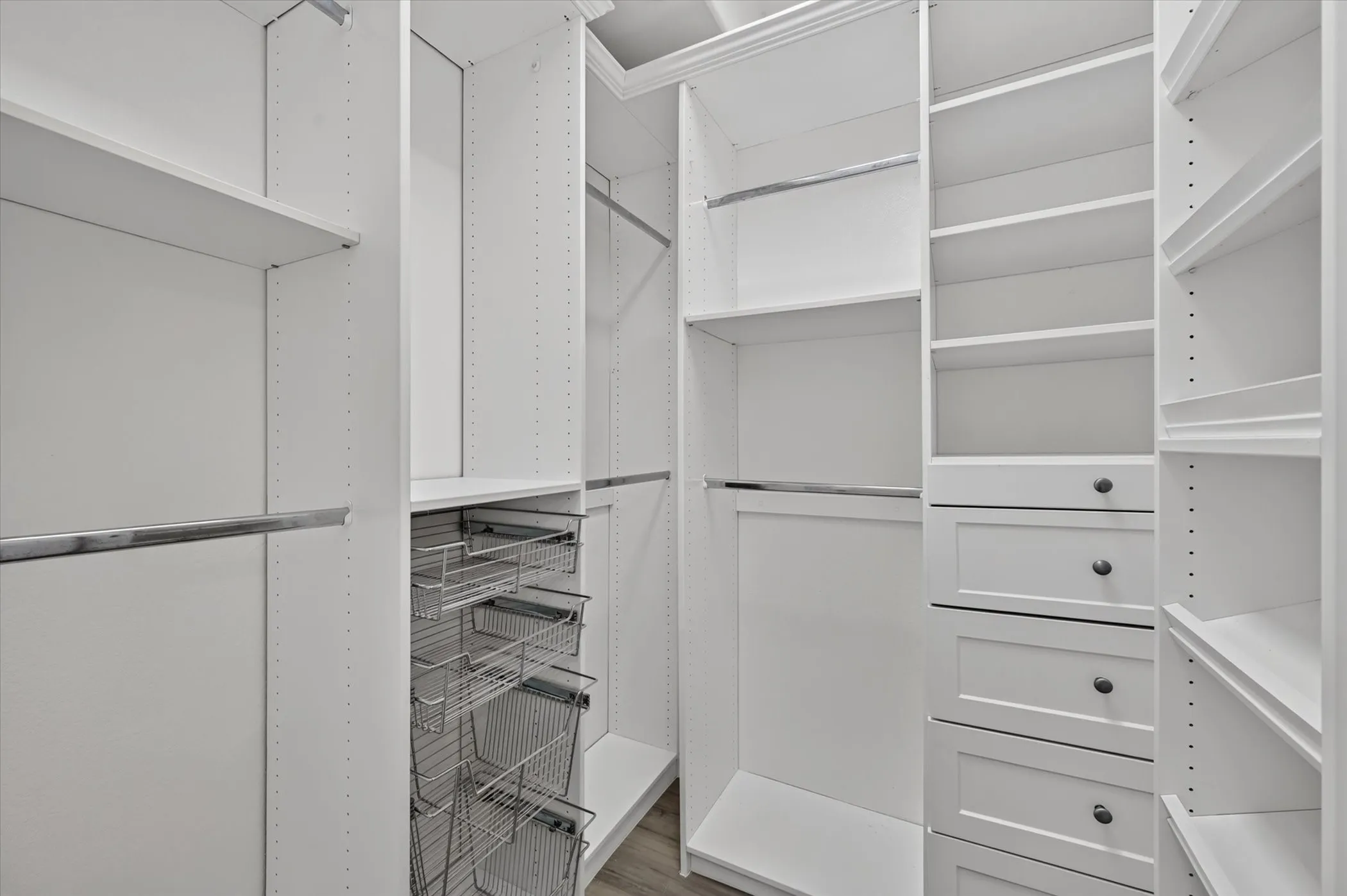 Custom white built-in closet system featuring adjustable shelving, integrated drawers with dark hardware, chrome hanging rods, and pull-out wire baskets