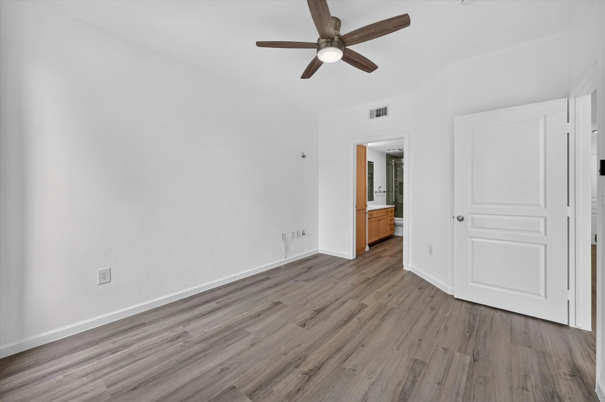 Spacious room featuring wood-finish flooring, a contemporary ceiling fan, and white baseboards