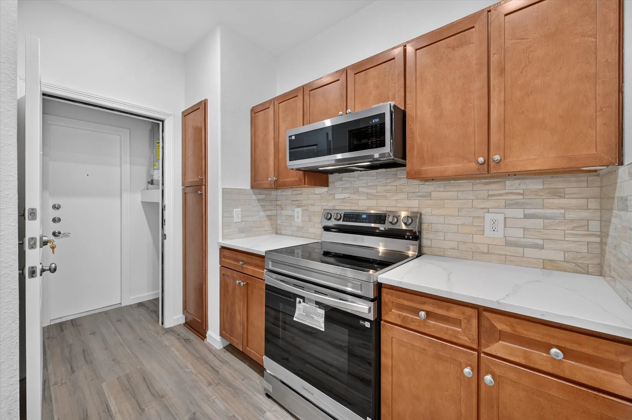Kitchen featuring wood-finish cabinetry, stainless steel appliances, light-toned tiled backsplash, and white countertops
