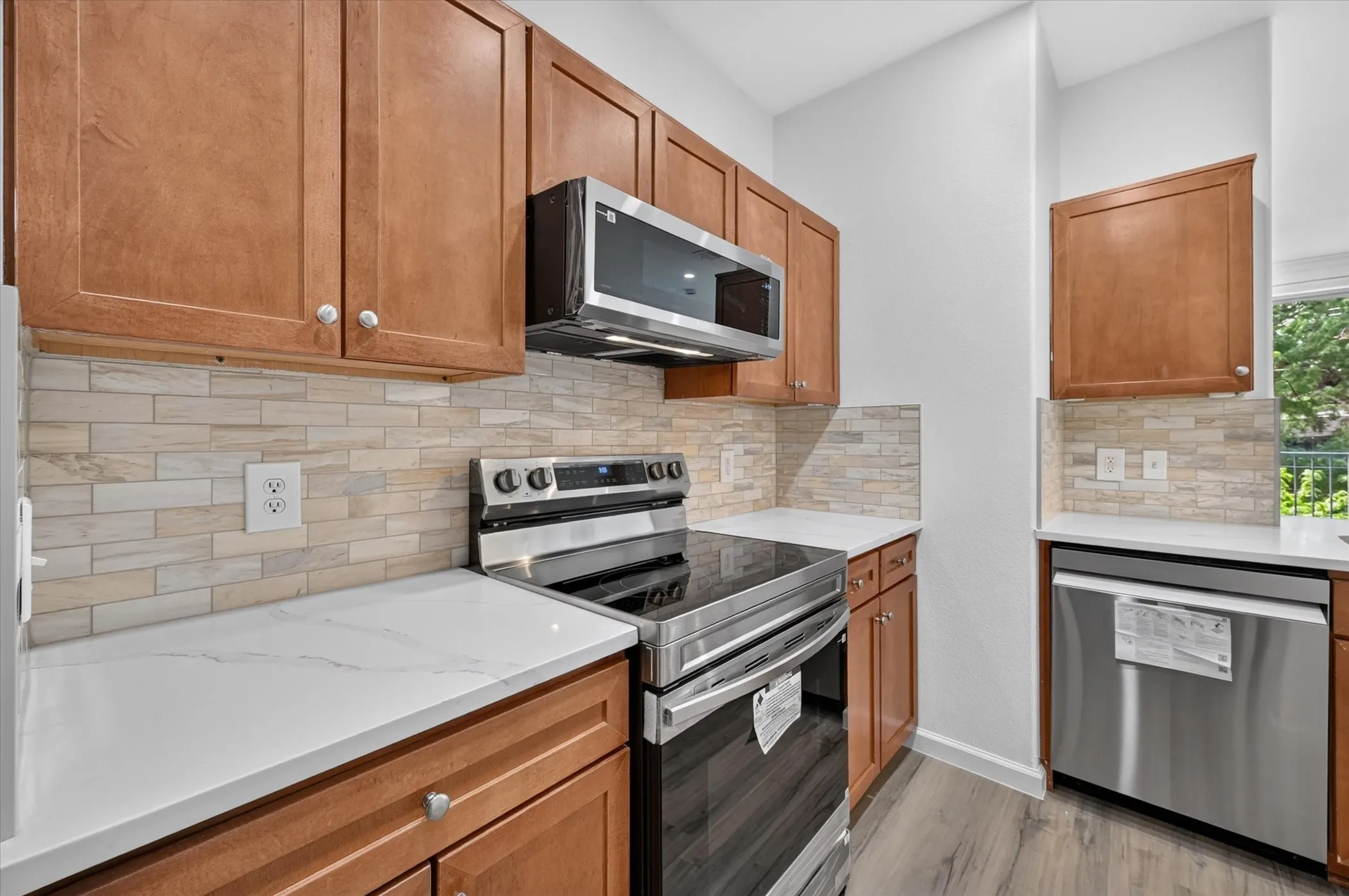 Kitchen featuring wood-finish cabinetry, stainless steel appliances, white quartz-finish countertops, and a subway tile backsplash