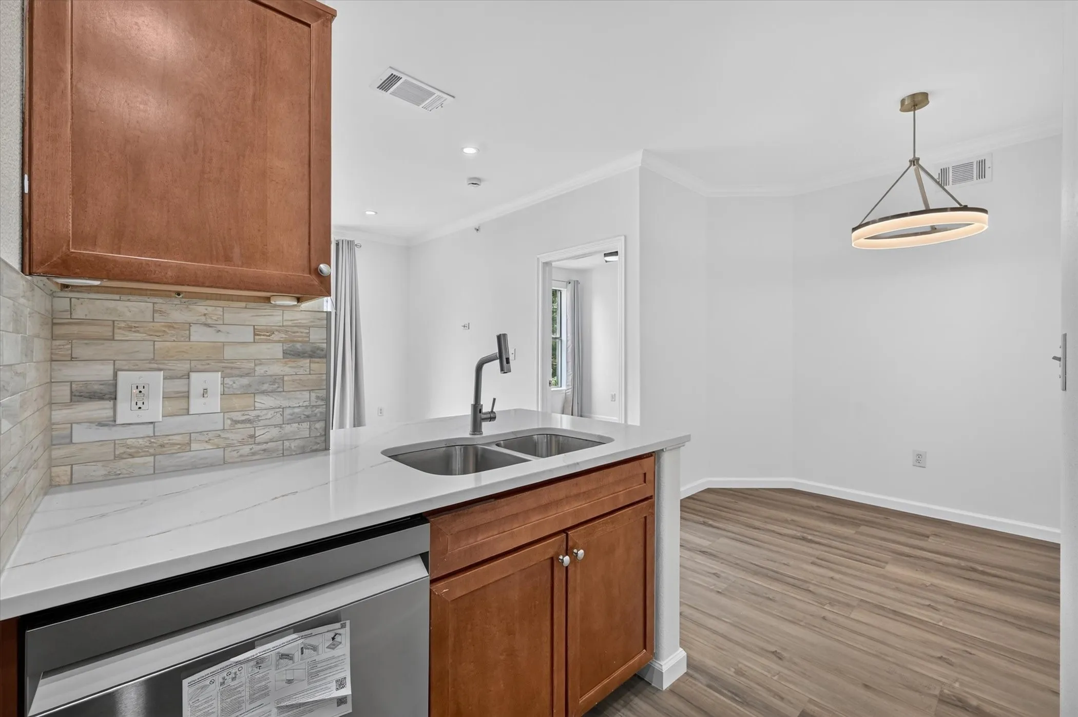 Kitchen island featuring a double basin stainless steel sink with a matte black faucet, white countertop, and integrated stainless steel dishwasher