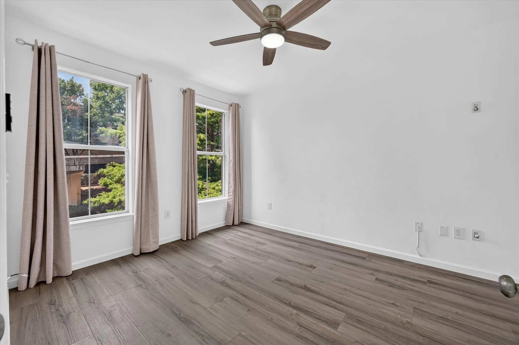 Spacious room featuring wood-finish flooring, white walls, and a ceiling fan