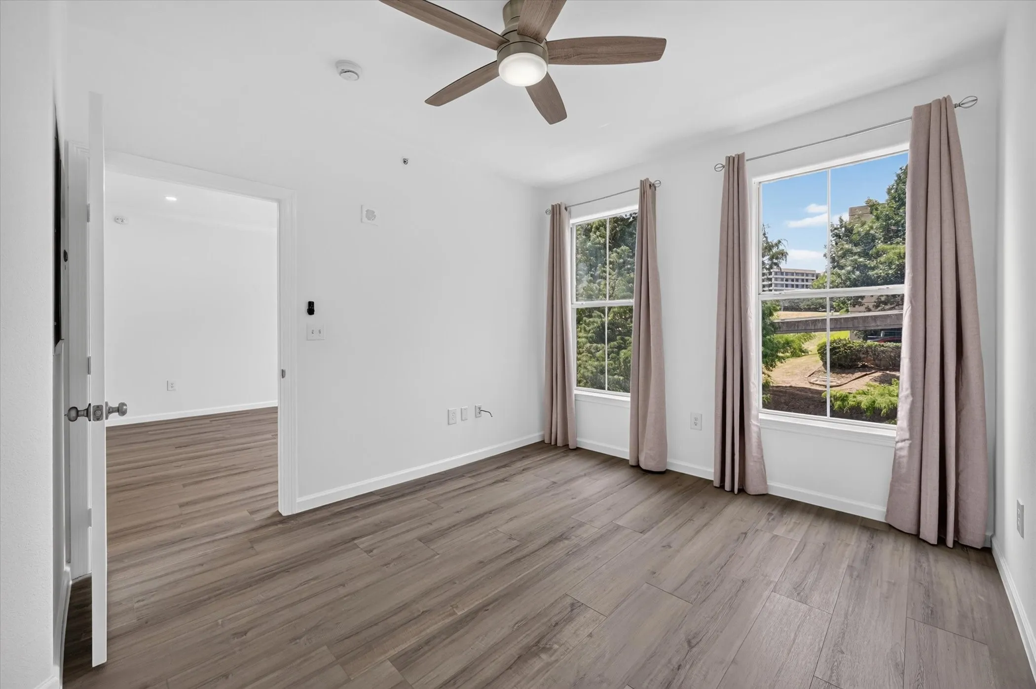 Spacious room featuring wood-finish flooring, a ceiling fan, and two large windows