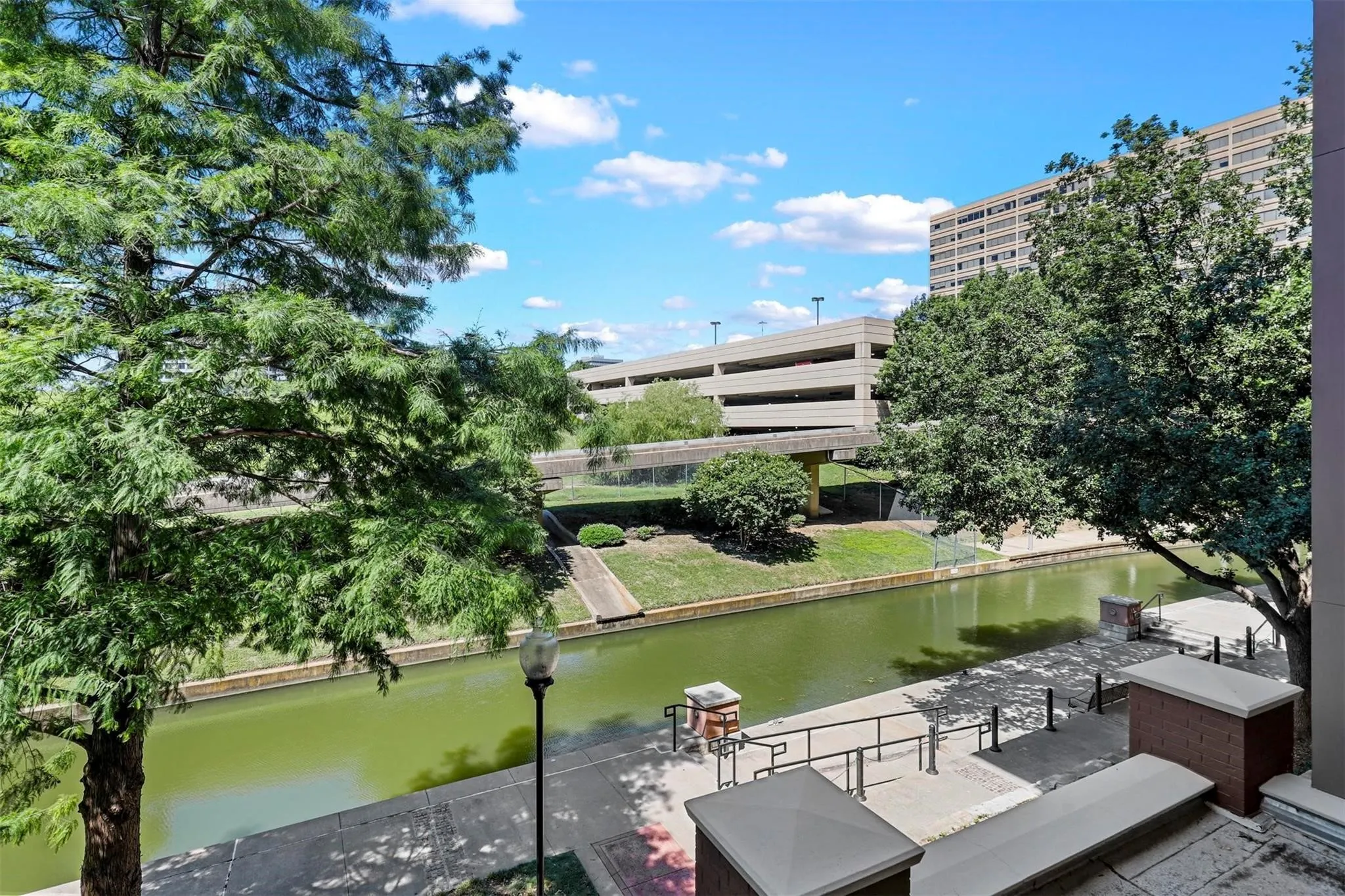 Canal-front setting with established trees, concrete walkways, and an adjacent parking structure