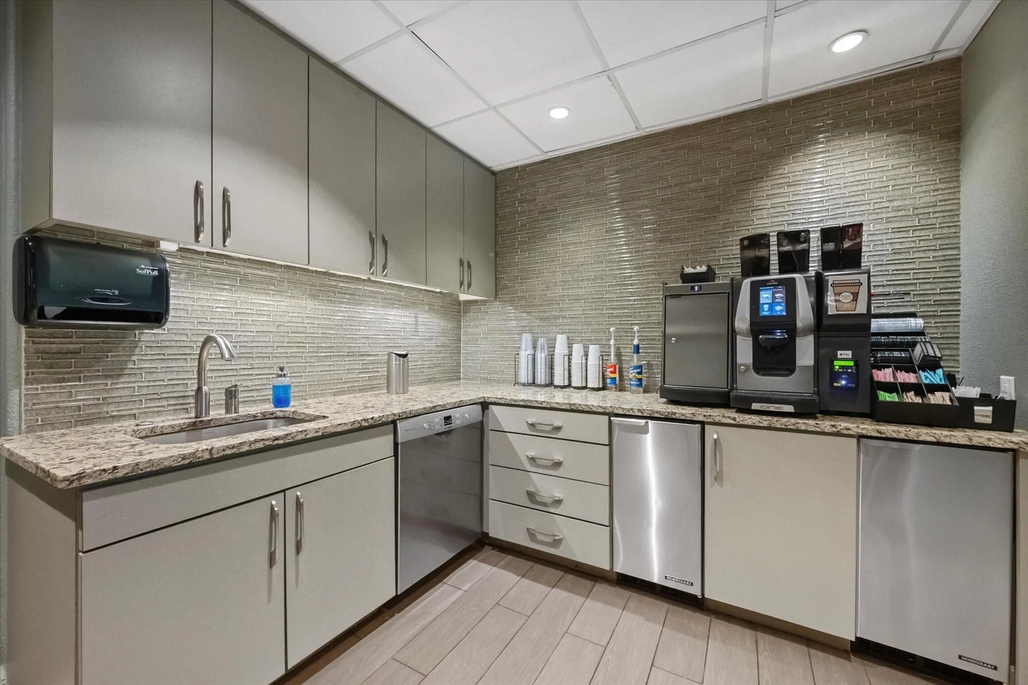 Contemporary kitchenette featuring extensive cabinetry, L-shaped stone countertops, and a full-height mosaic tile backsplash