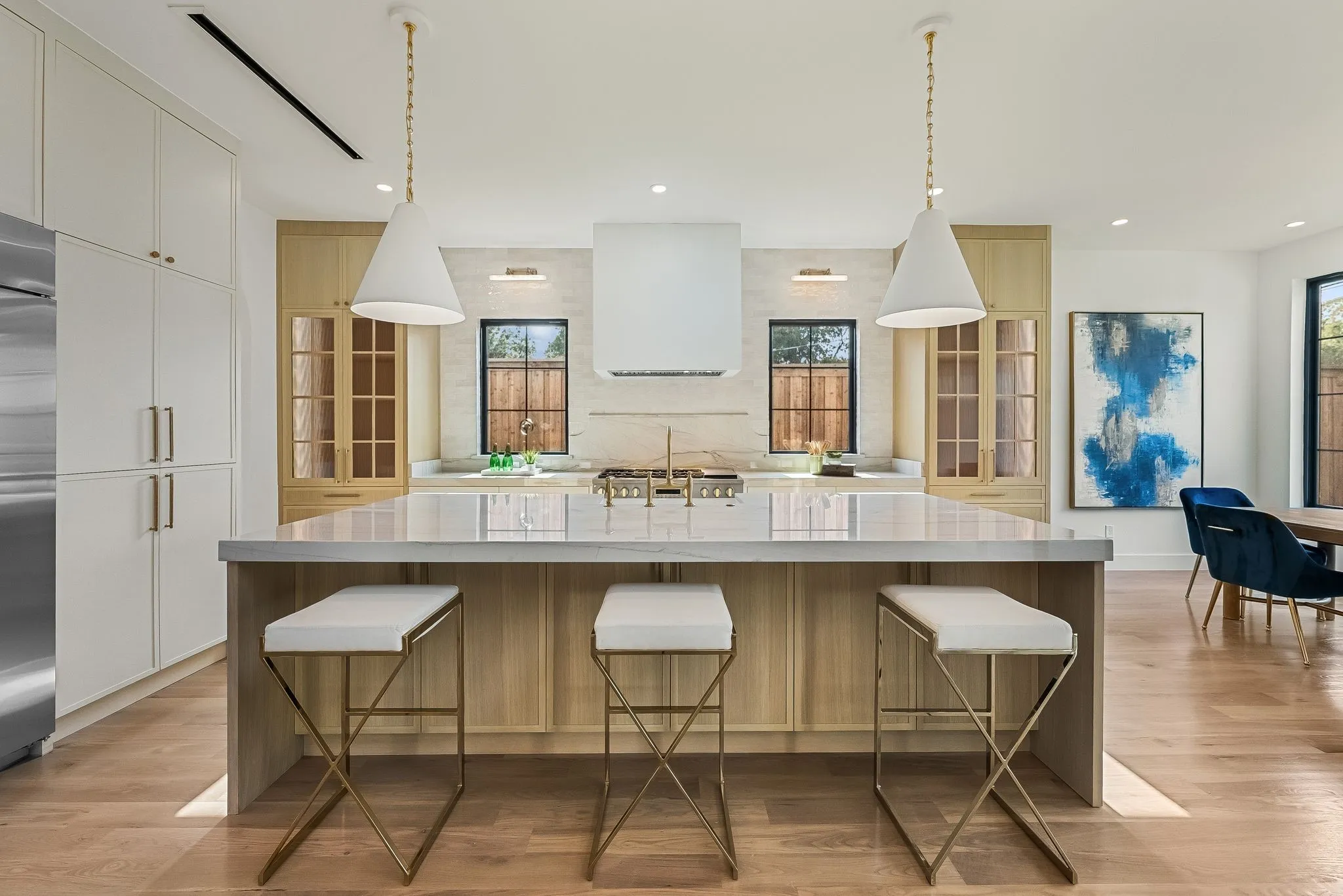 Gourmet kitchen featuring a substantial island with seating, a professional-grade range with a built-in ventilation hood, wood-finish flooring, full-height cabinetry, and architectural pendant lighting