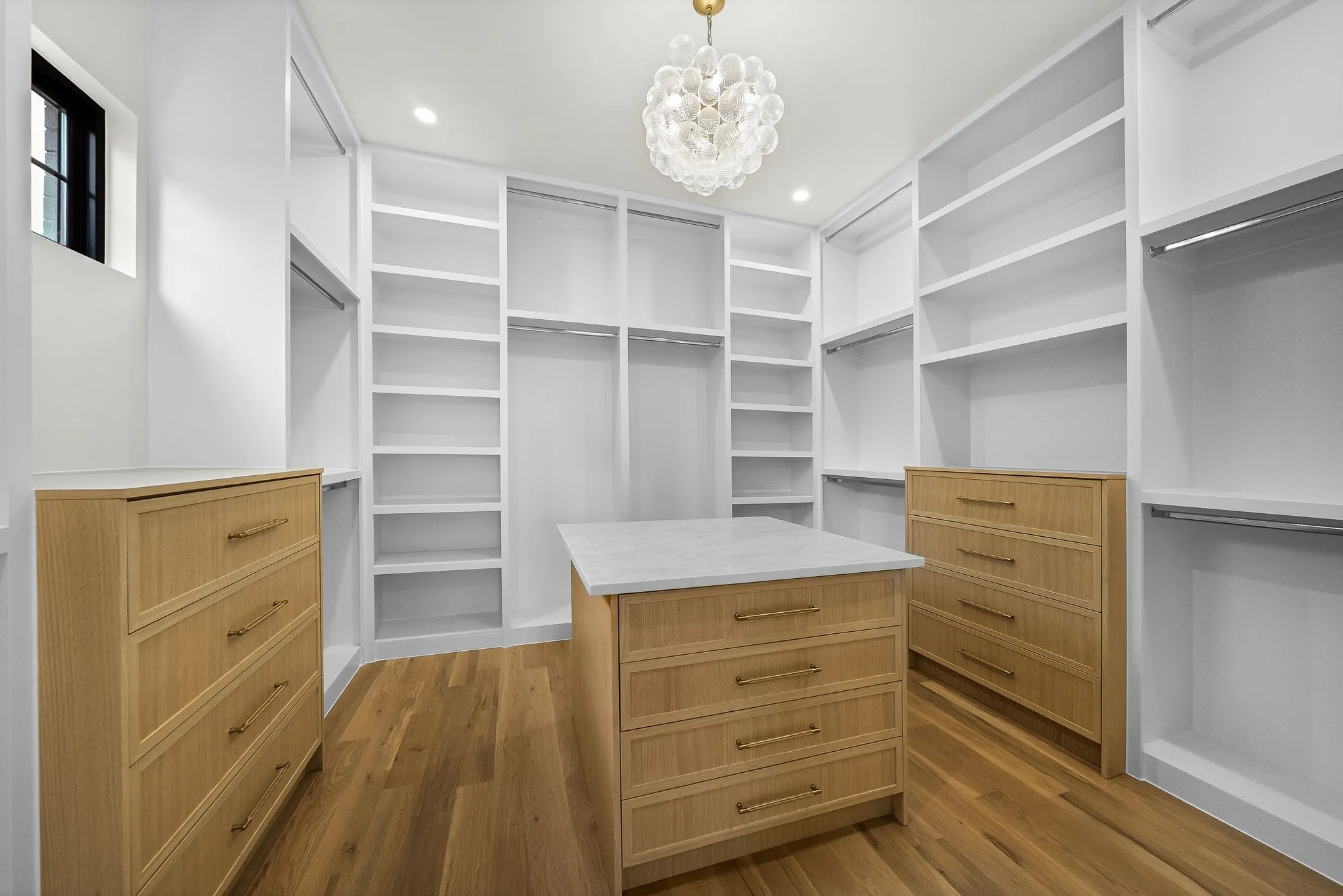 Spacious custom closet featuring extensive built-in shelving, hanging rods, two integrated dressers, a central island with countertop, and wood-finish flooring